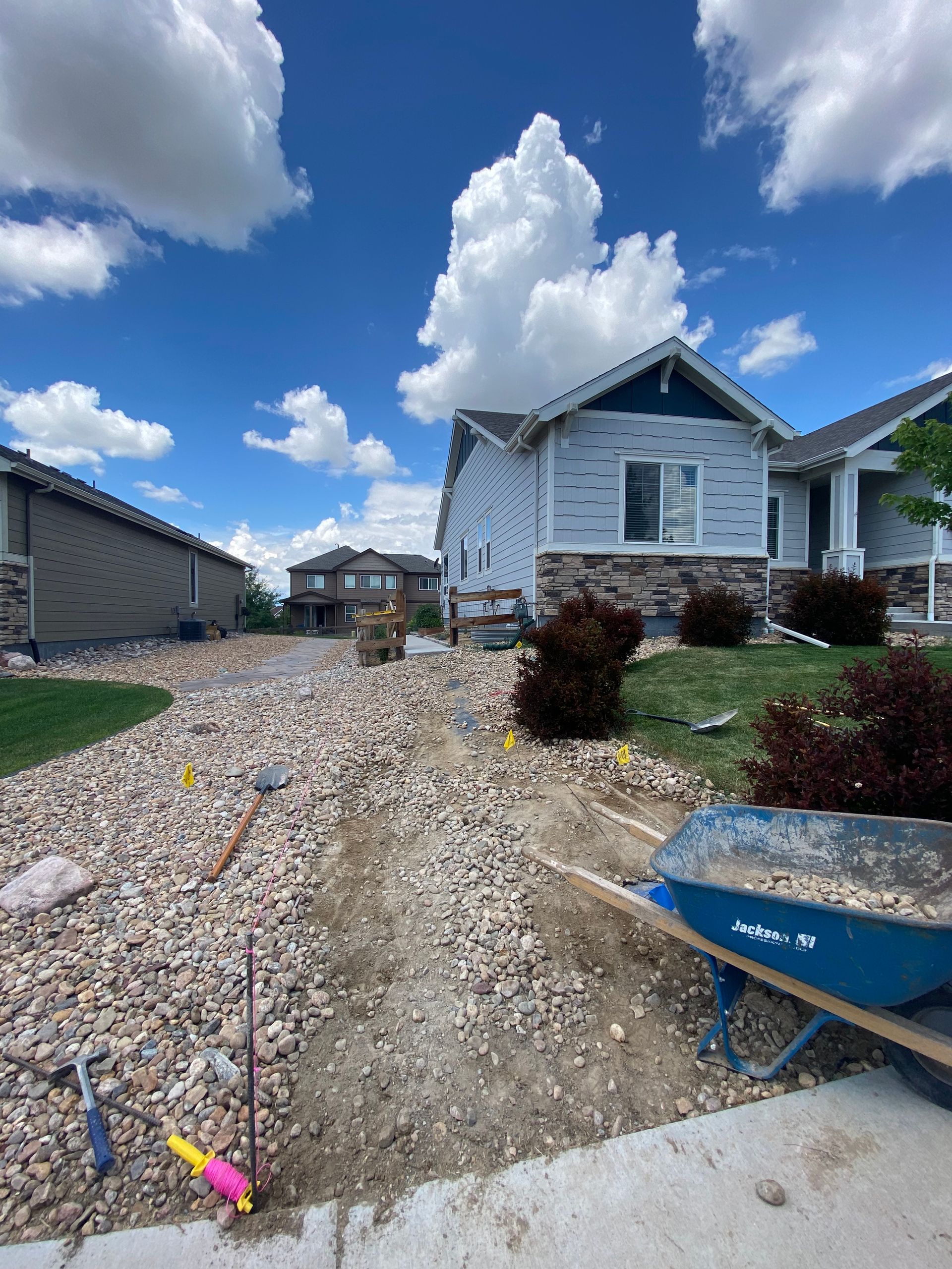Residential construction site with gravel driveway, house, blue sky, and wheelbarrow.
