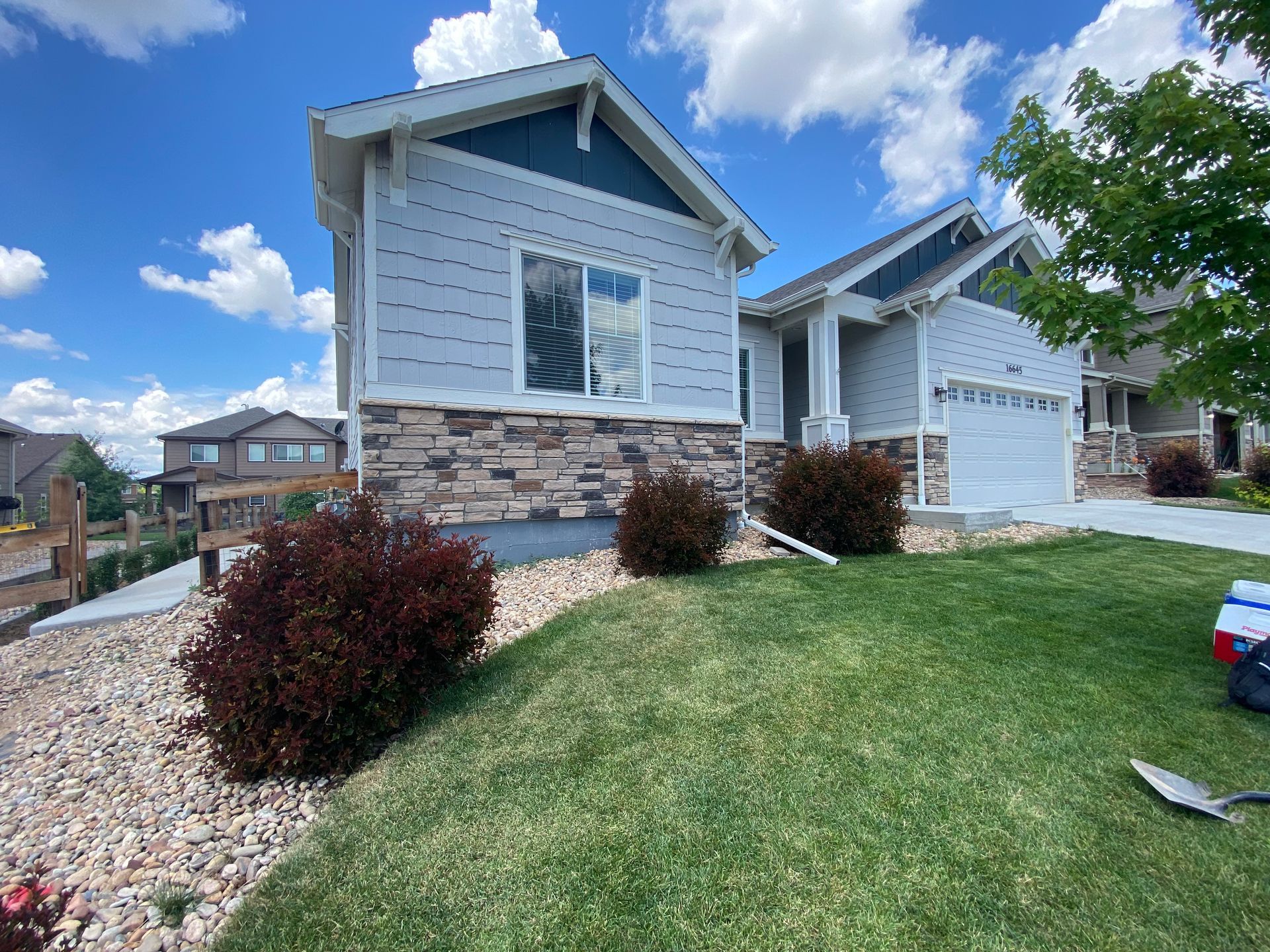 House exterior with blue siding, stone accents, and green lawn under a blue sky.