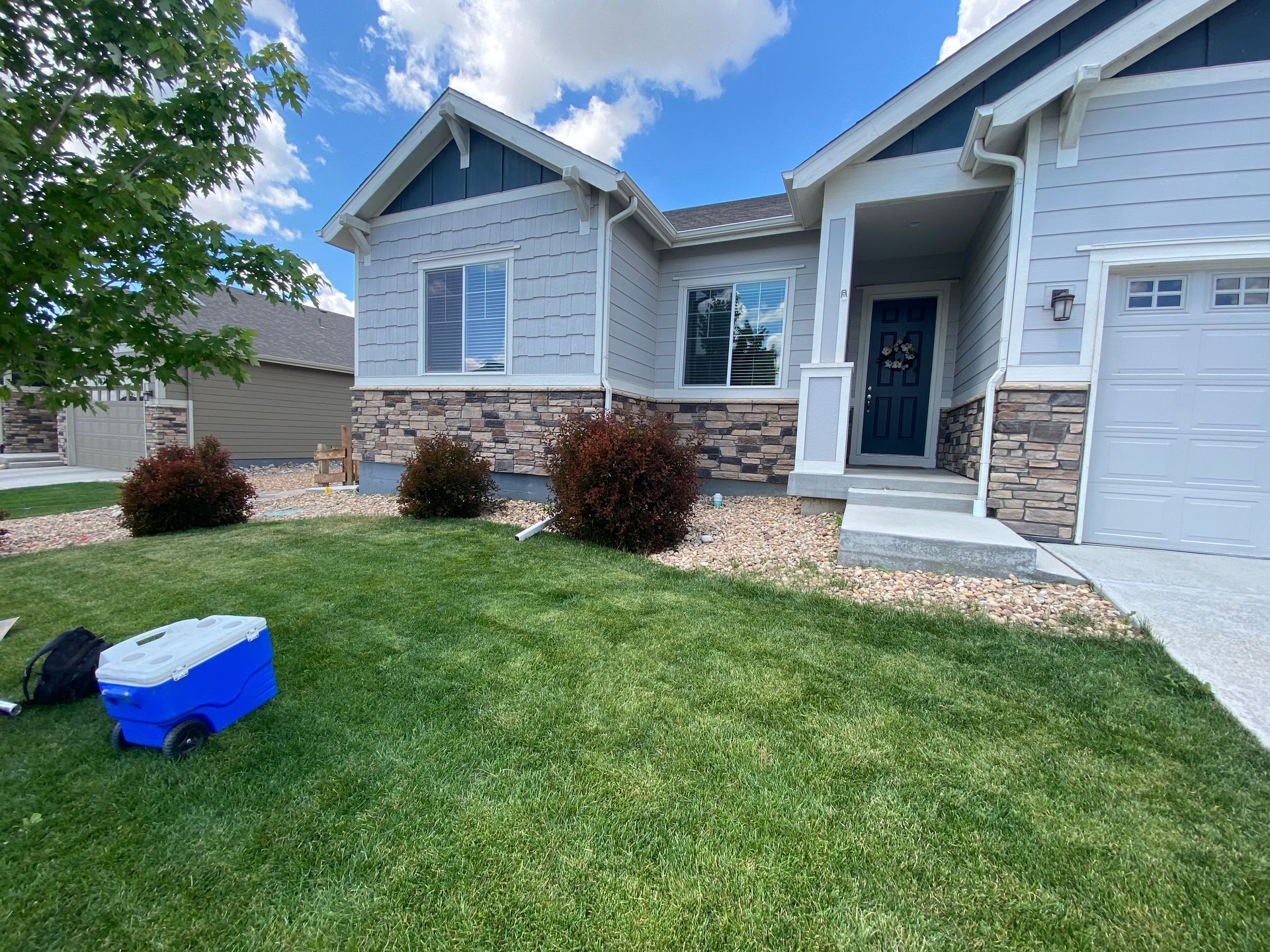 A light gray house with stone accents, blue door, and green lawn under a partly cloudy sky.