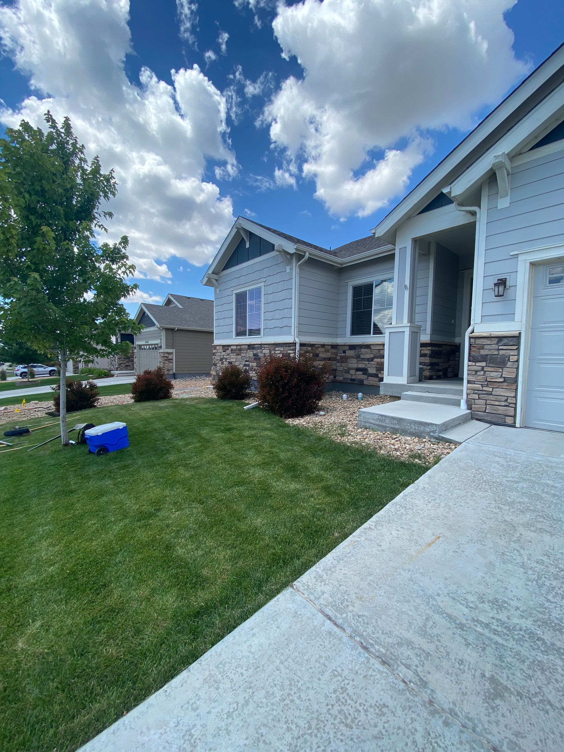 Gray house with stone accents, blue sky, green lawn.