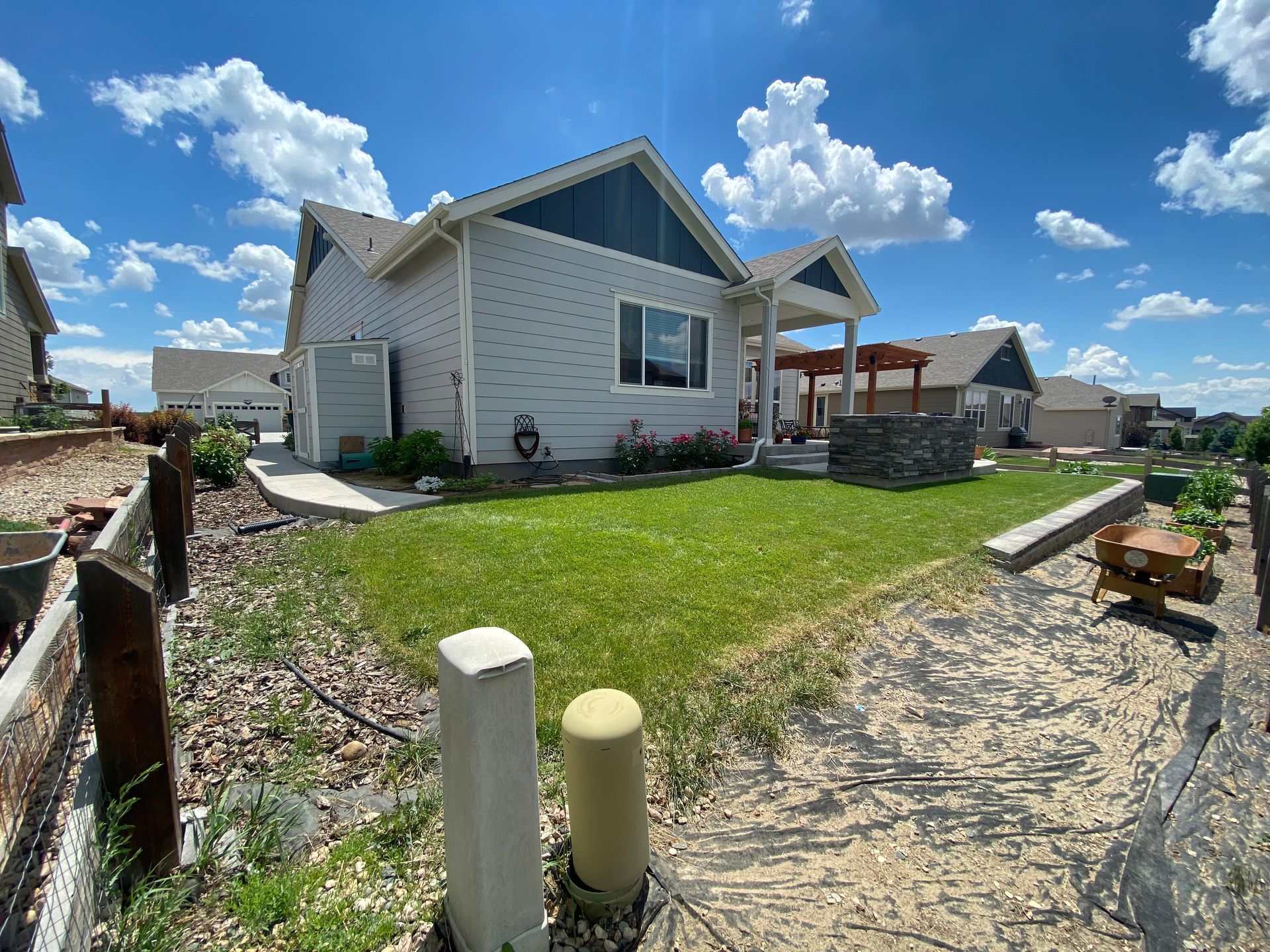 Light gray house with blue accents, green lawn, blue sky with puffy clouds.