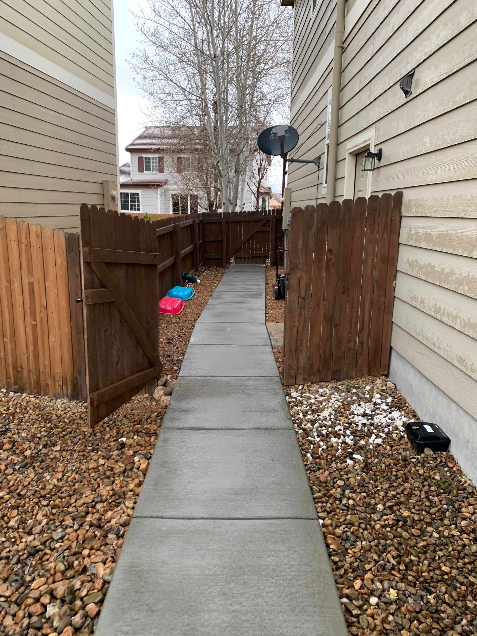 A narrow concrete walkway between buildings, enclosed by brown fences. Gravel on either side.