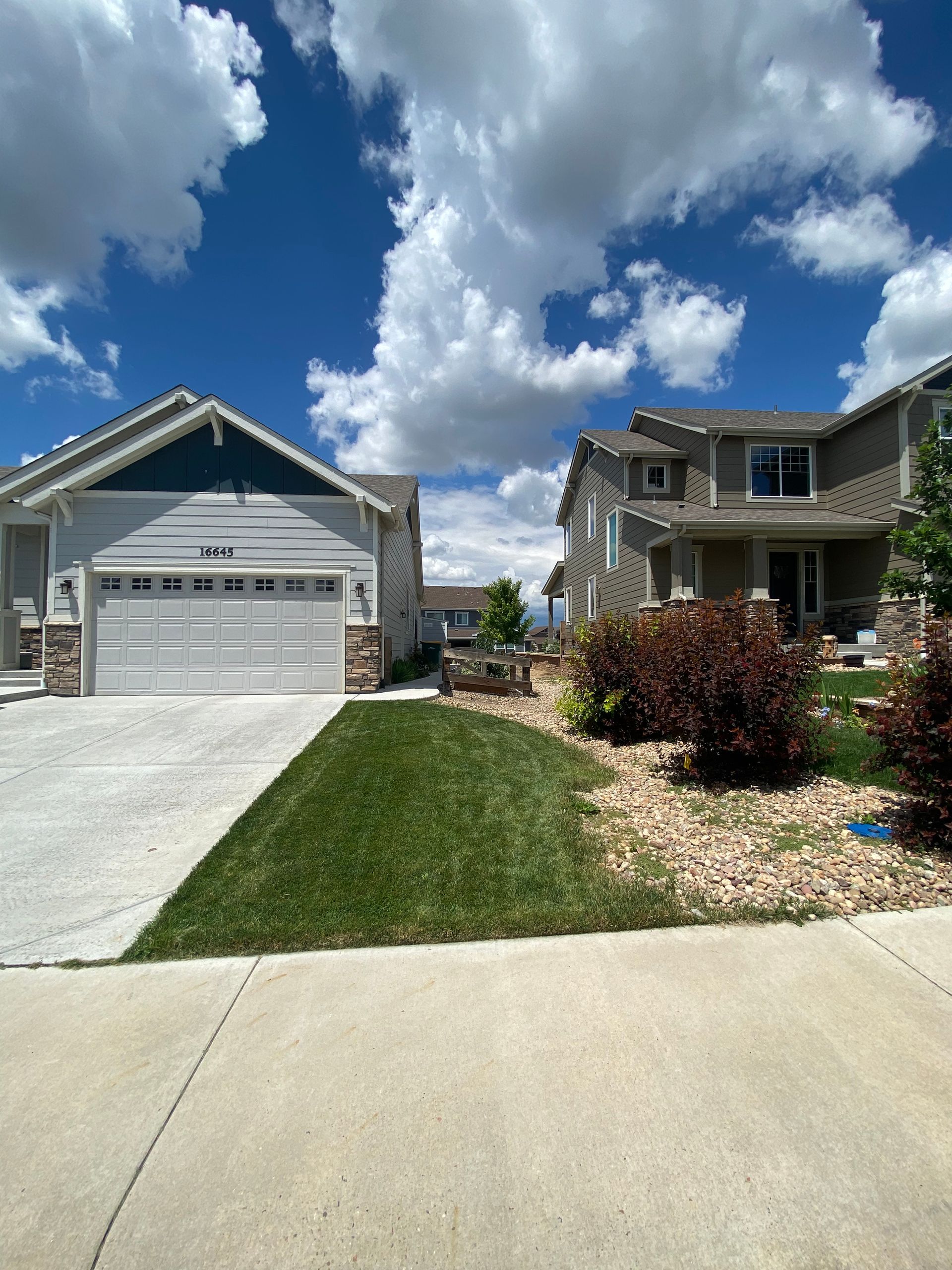 Two houses with light blue siding and a well-manicured lawn under a bright blue sky with puffy white clouds.