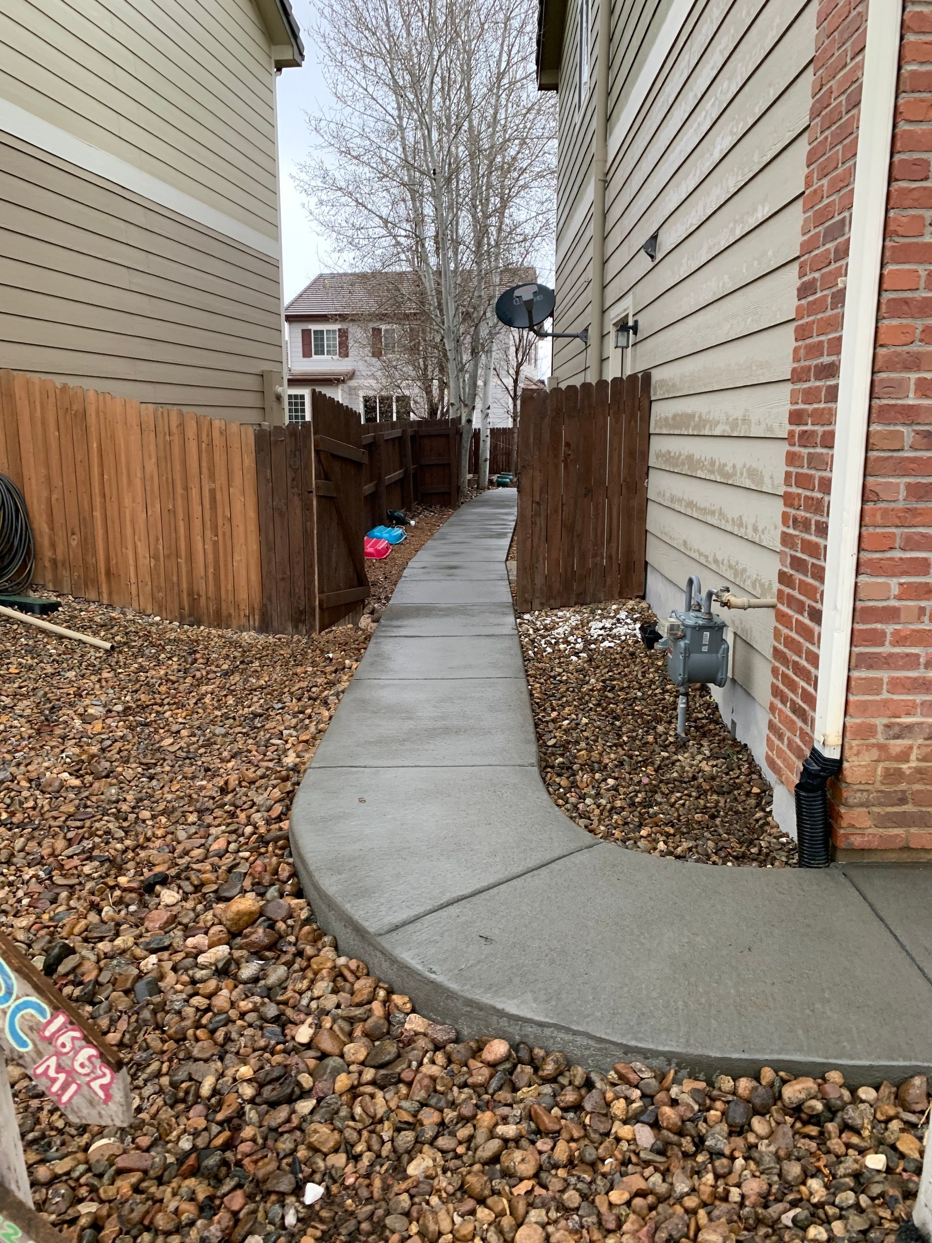 Concrete path between two buildings, bordered by wooden fence and rocks.