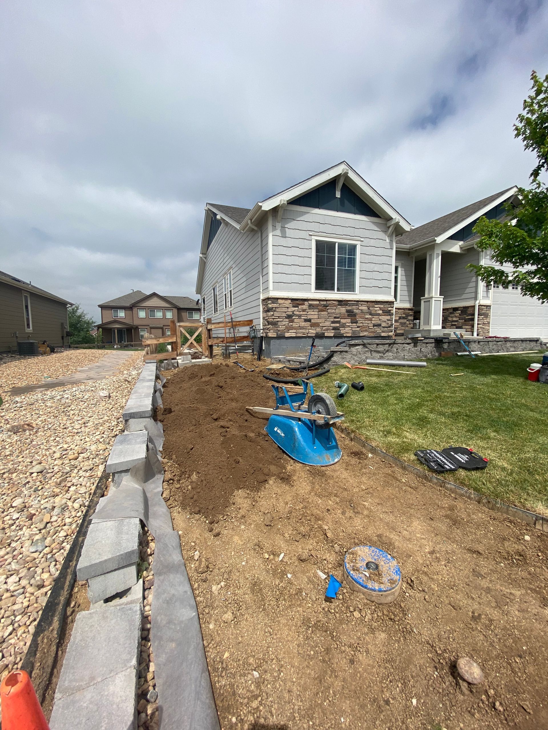 A house under construction with a stone retaining wall, dirt, and construction equipment in a yard.