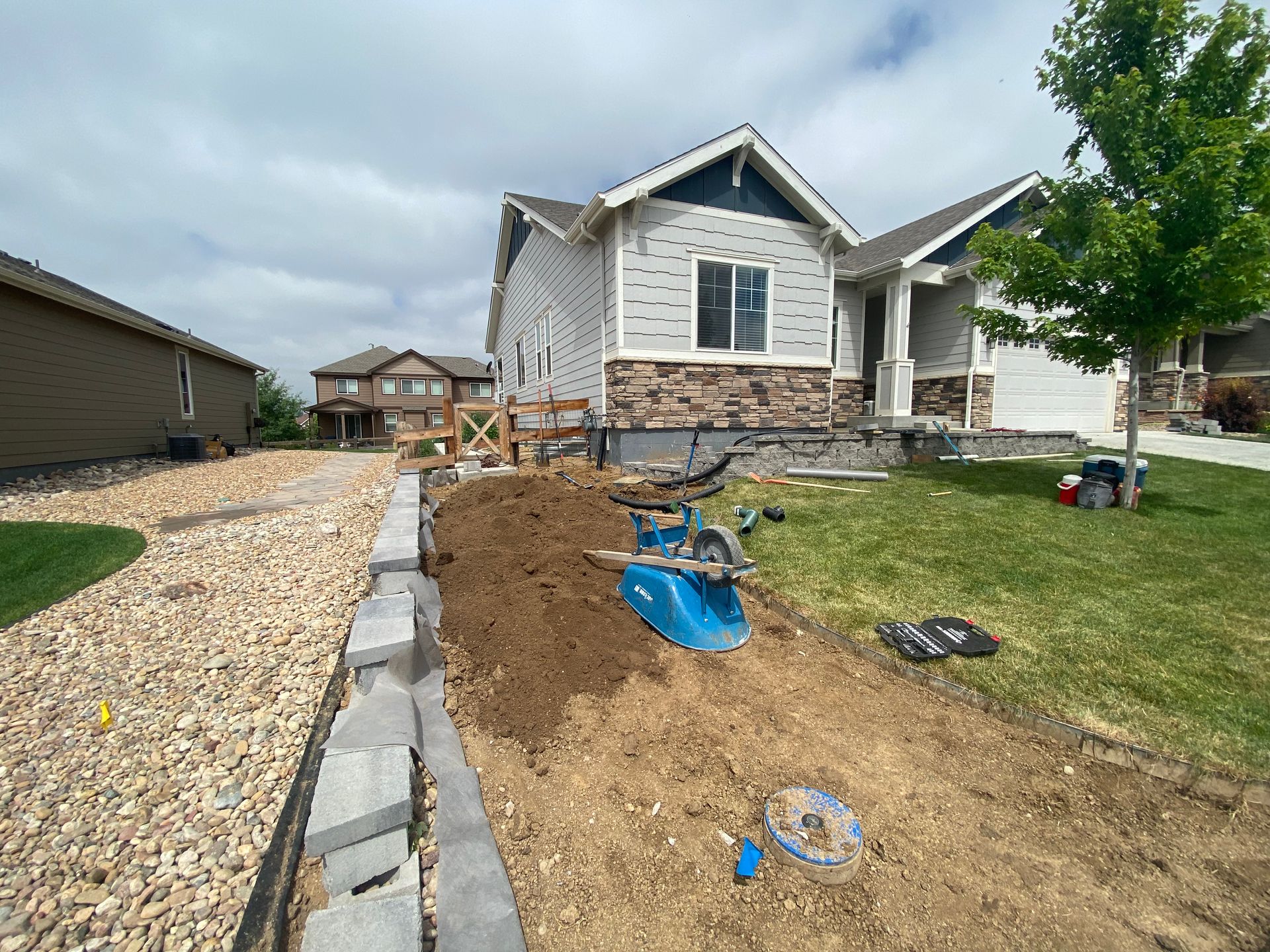 House with landscaping under construction: gravel path, soil pile, retaining wall, and lawn.