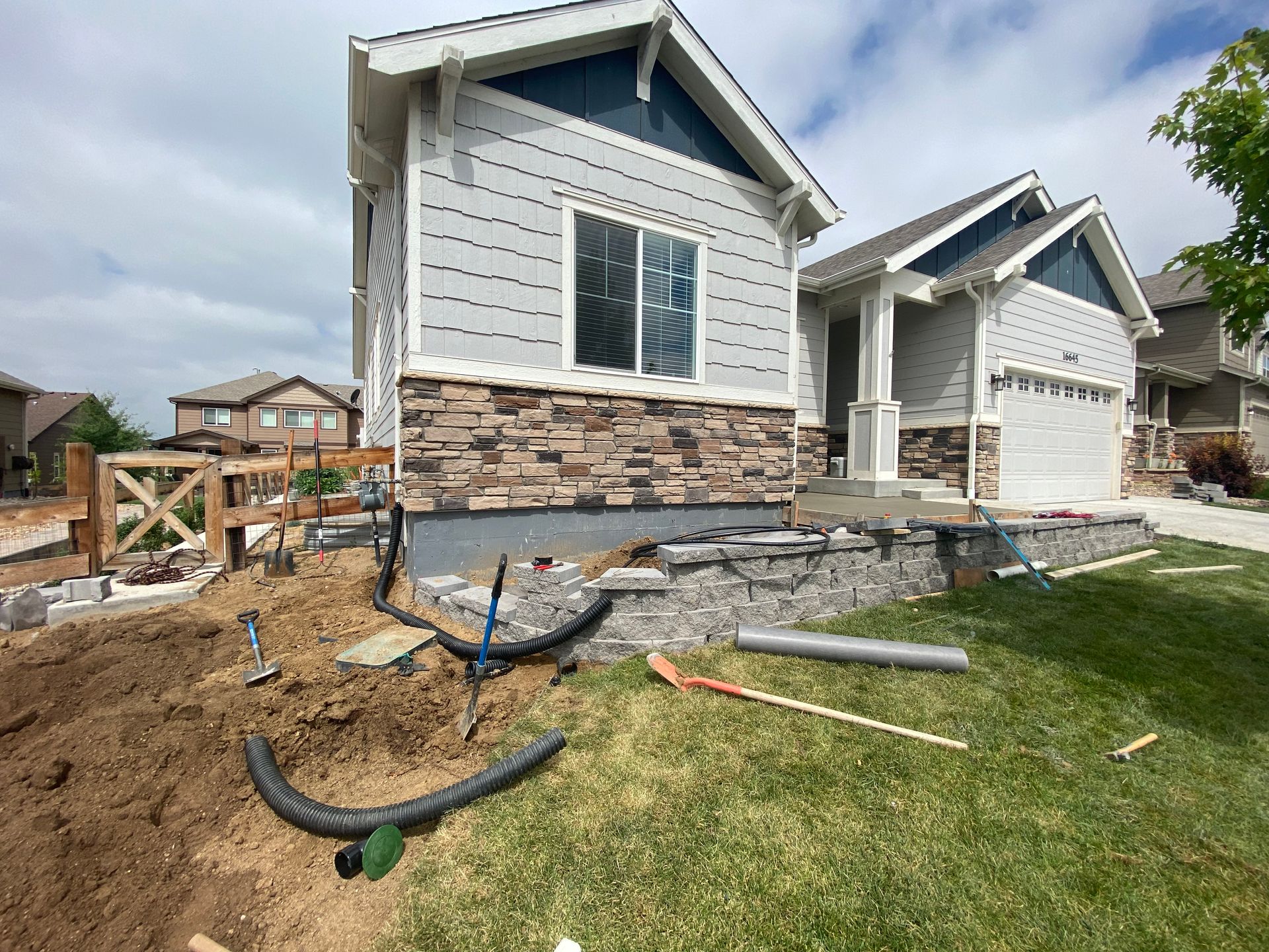House under construction; stonework, dirt, tools, and drainage pipes in yard.