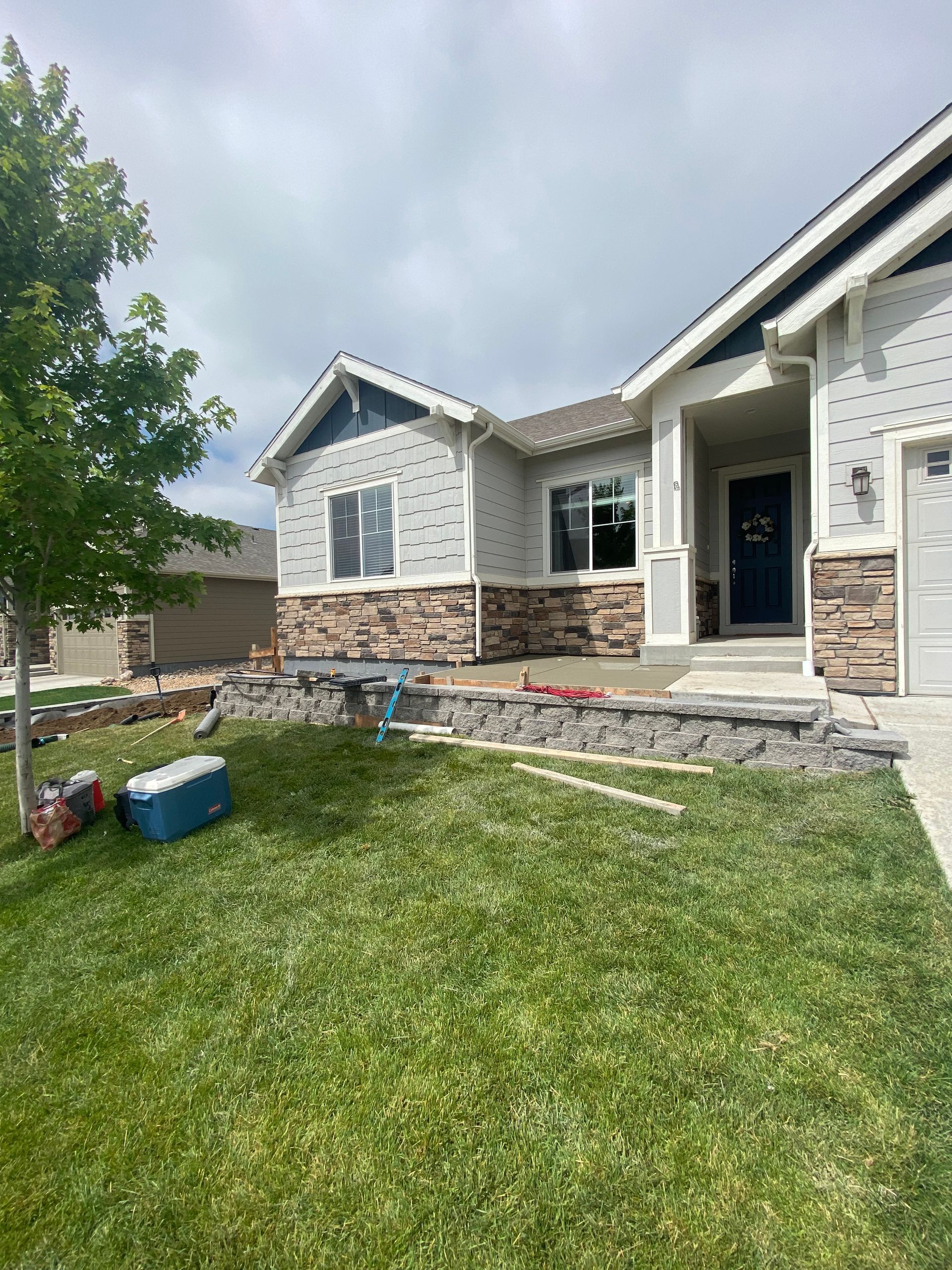 House exterior with stone accents and a low retaining wall; green lawn, cloudy sky.