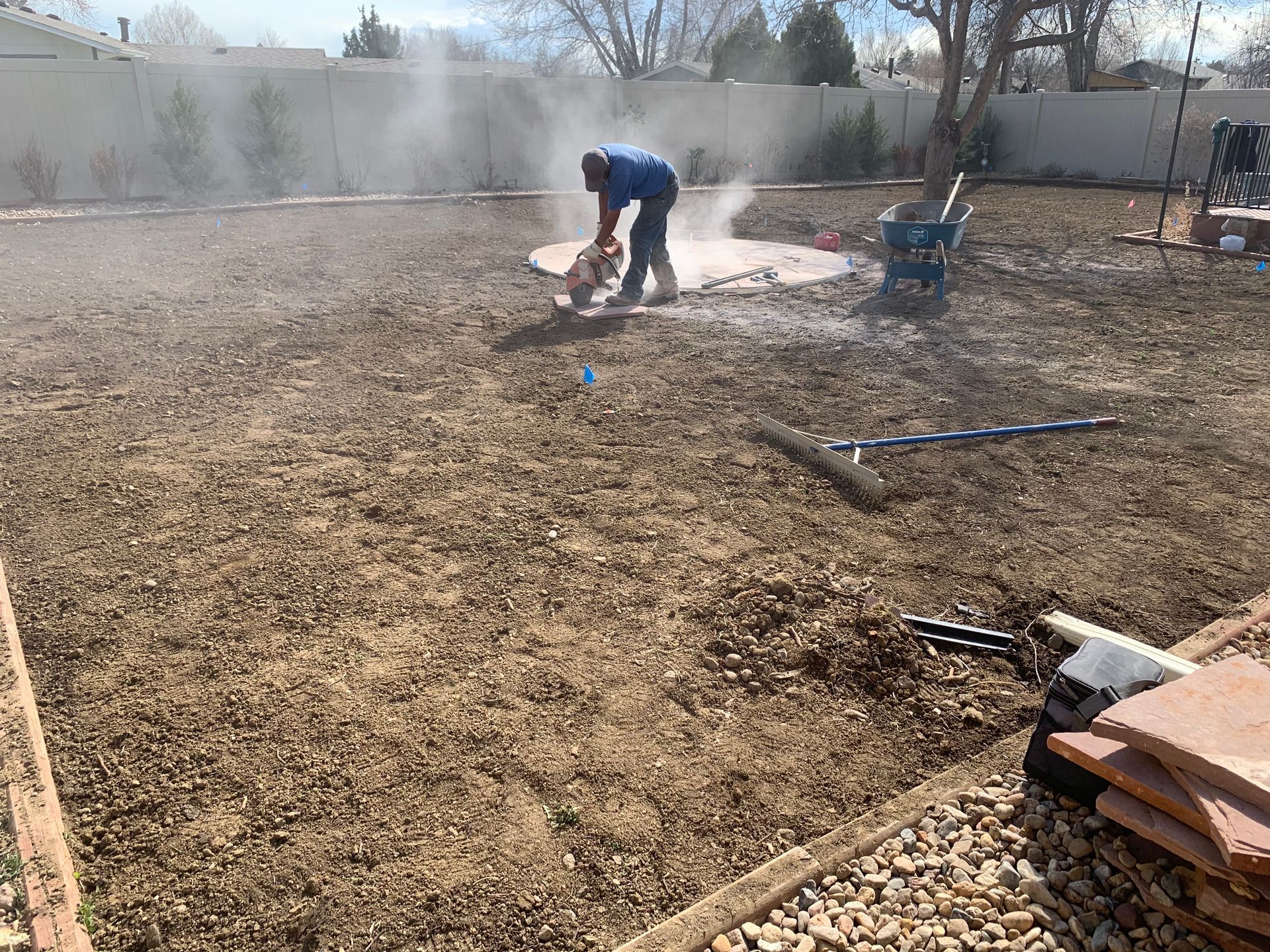 Person cutting concrete in a backyard, creating a fire pit. Dust is visible.