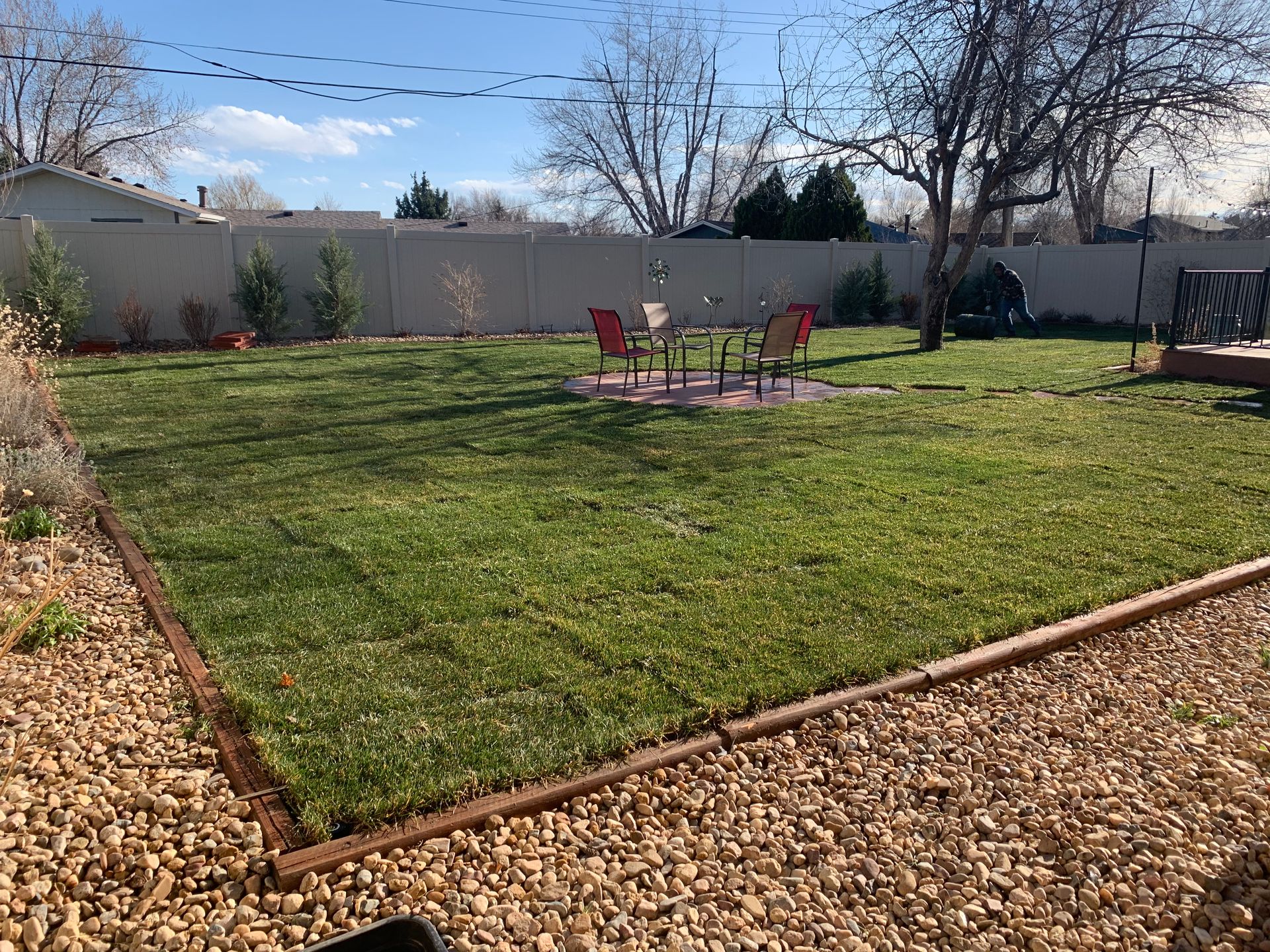 Backyard with green grass, gravel border, patio set, and tan fence.