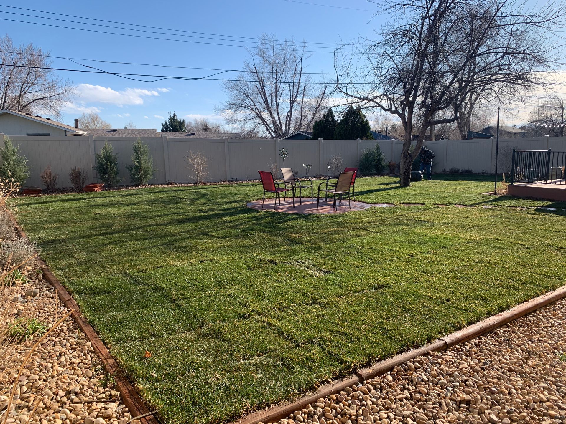 A backyard with green grass, a small table and chairs, and a gravel border.