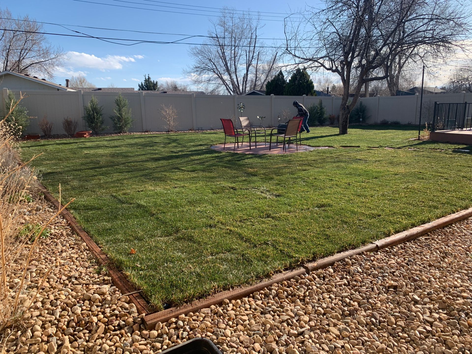 Well-kept backyard with green grass, a gravel border, and a person near a fire pit.