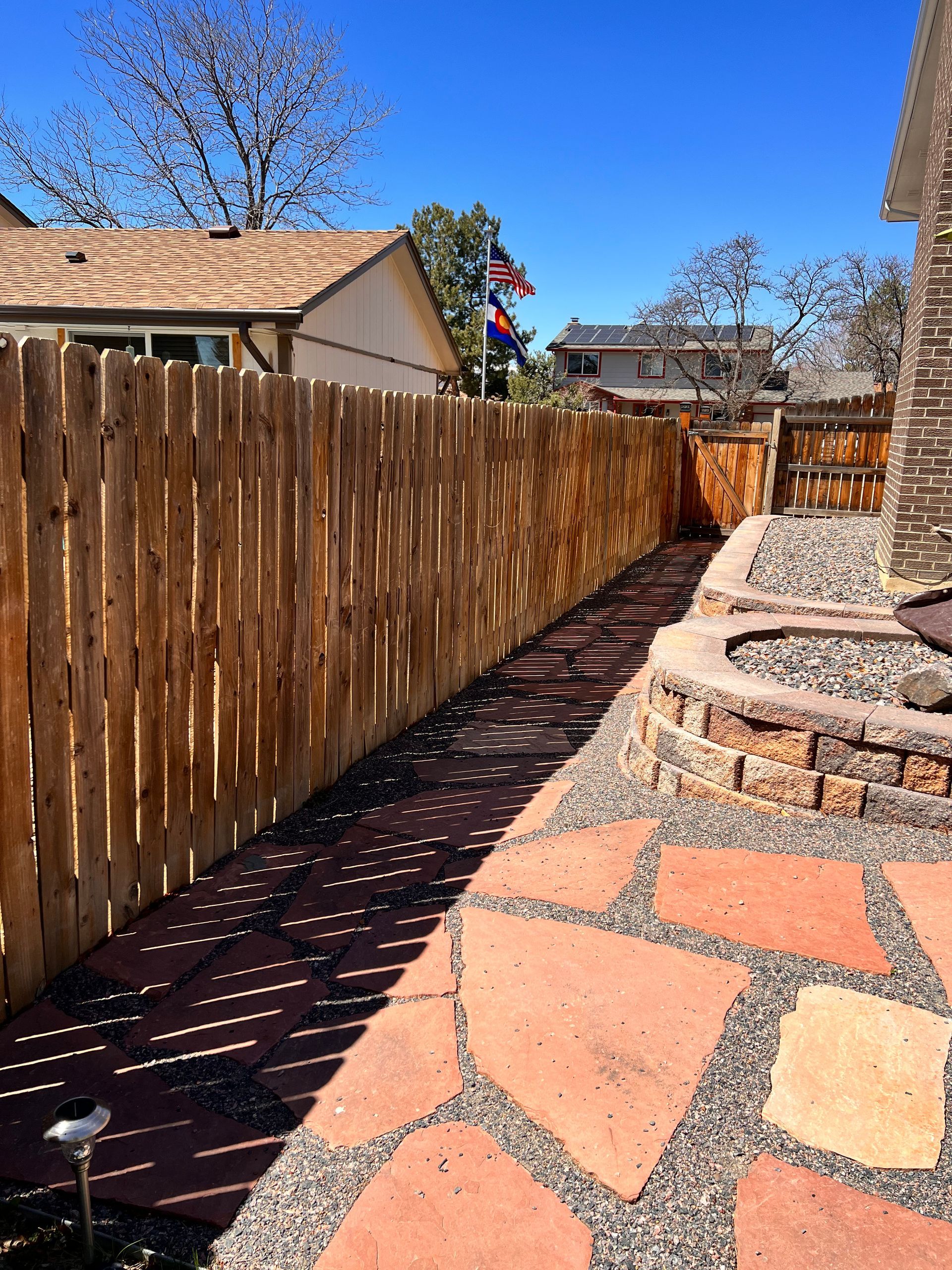 Stone patio and pathway with a wooden fence alongside a home.