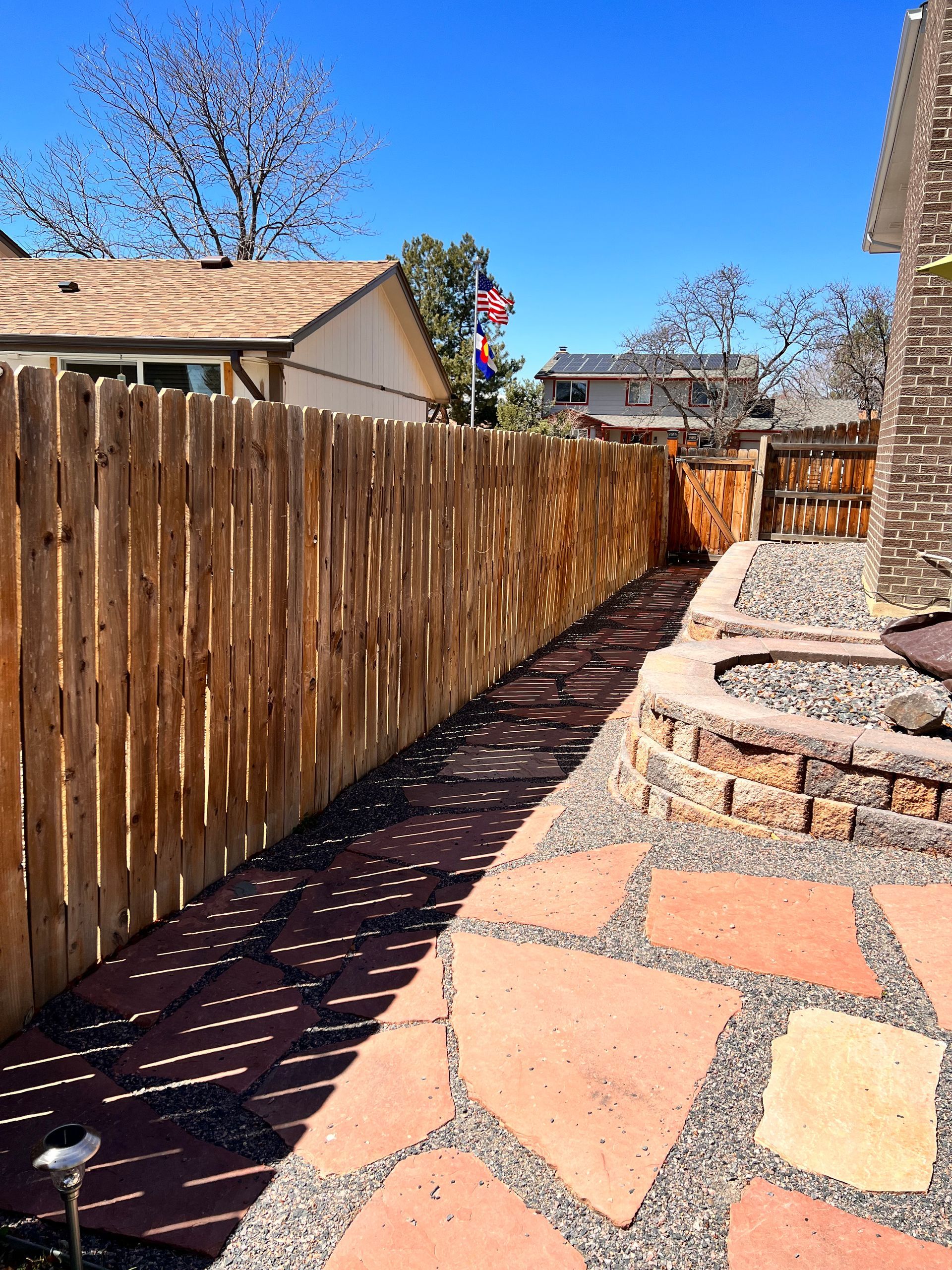 Backyard path of flagstone and gravel next to a wooden fence. Fire pit on right.