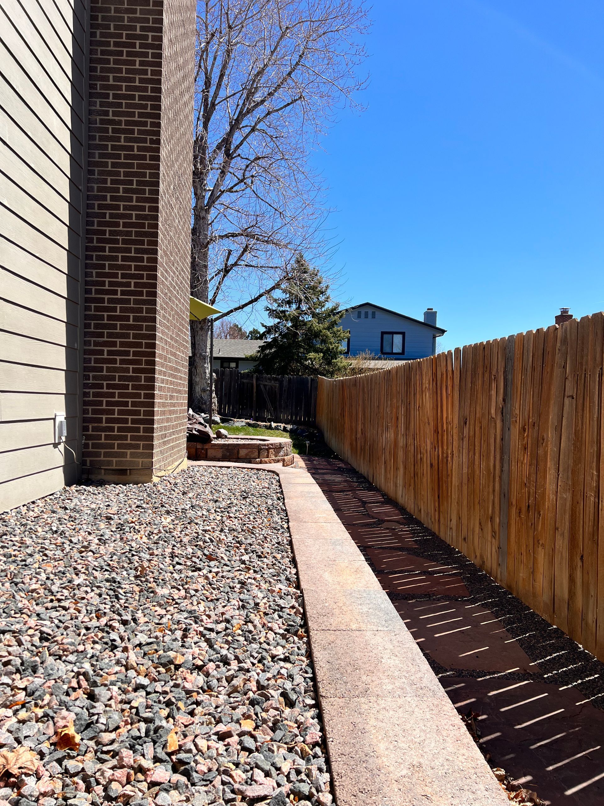 Side yard with brick chimney, gravel, walkway, wooden fence, and blue sky.