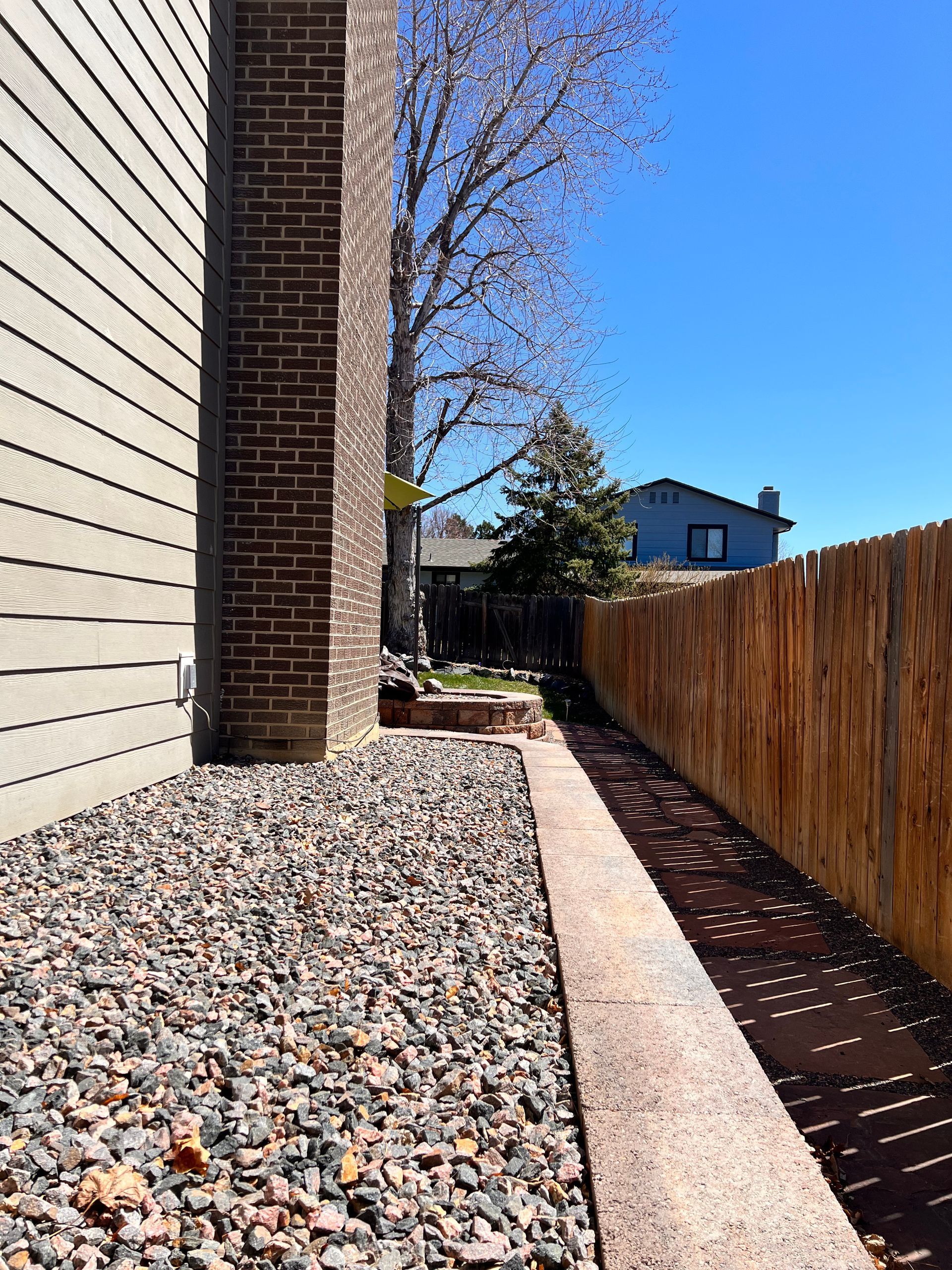 Gravel path and brick wall next to a wooden fence under a clear blue sky.