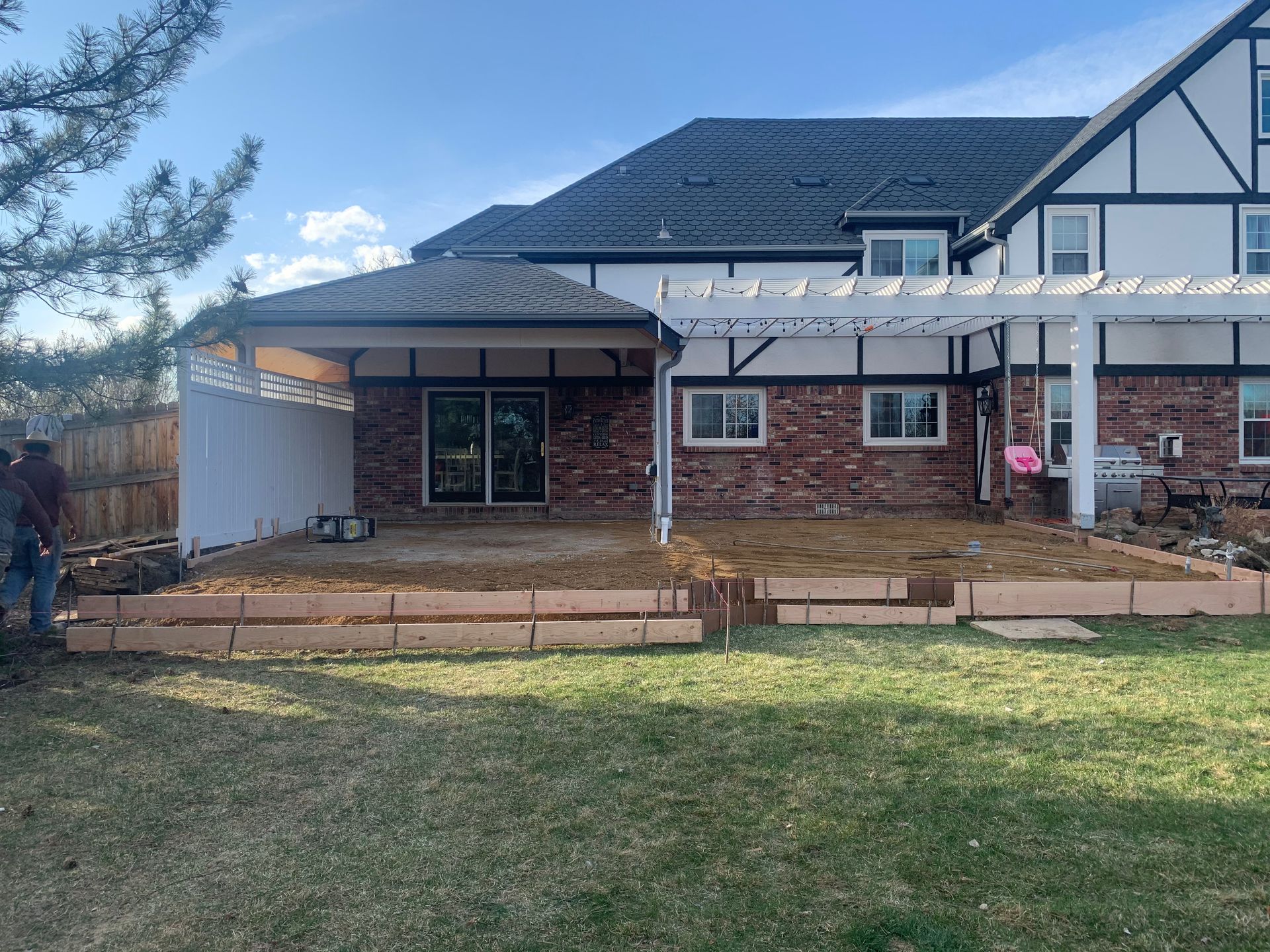 Backyard patio under construction with brick house and pergola.