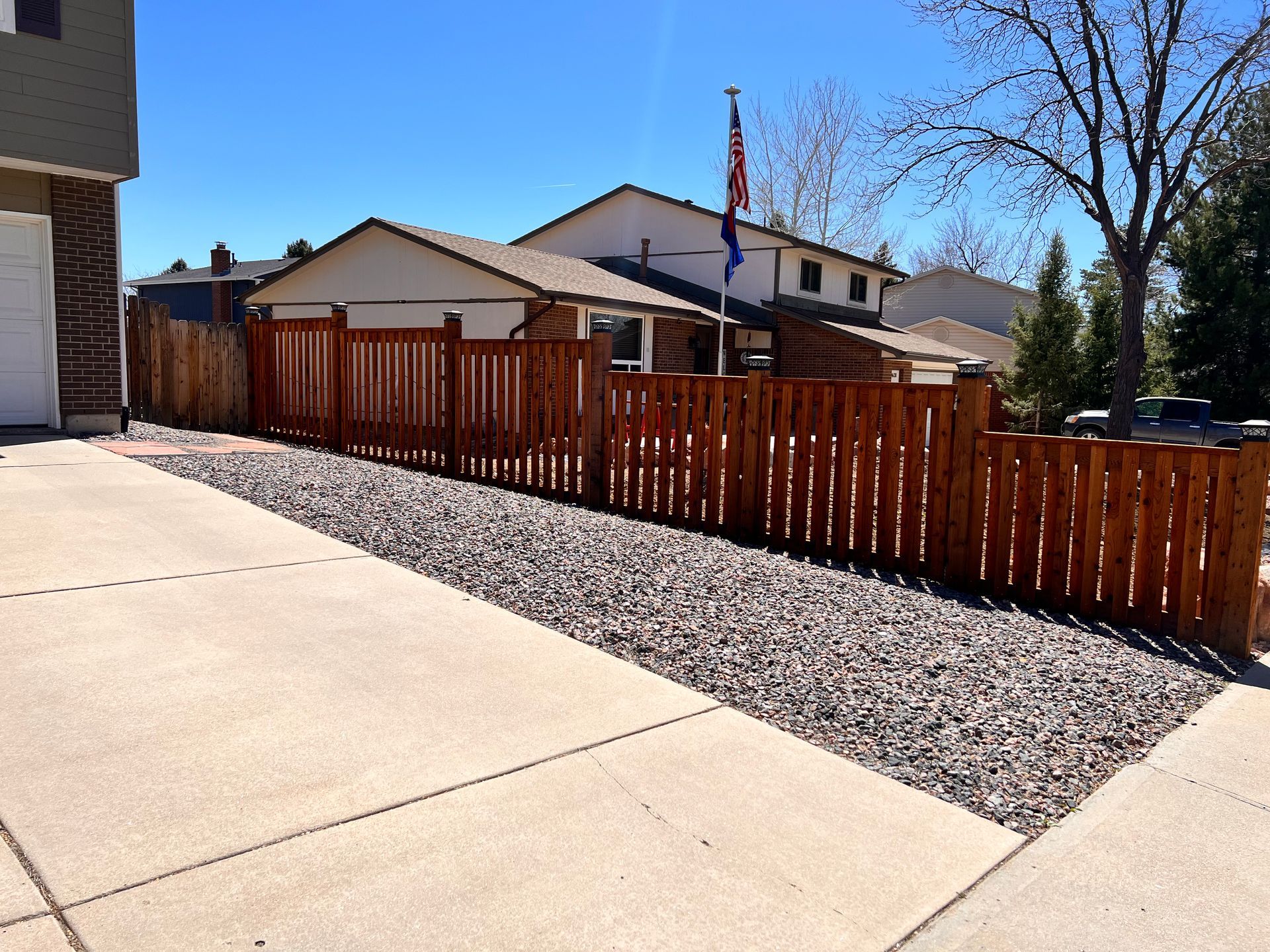 Wooden fence along a driveway with gravel, sunny day.