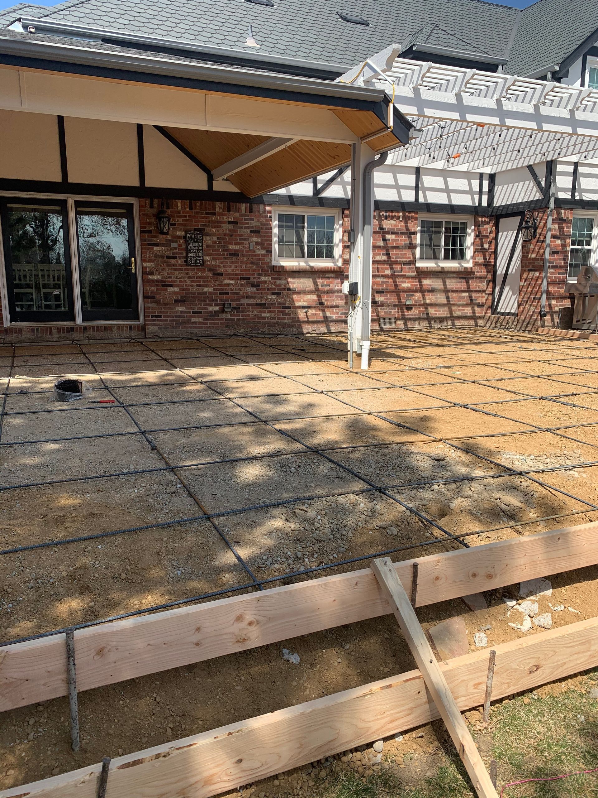 Patio under construction: wooden frame, metal grid, against brick wall, with pergola.