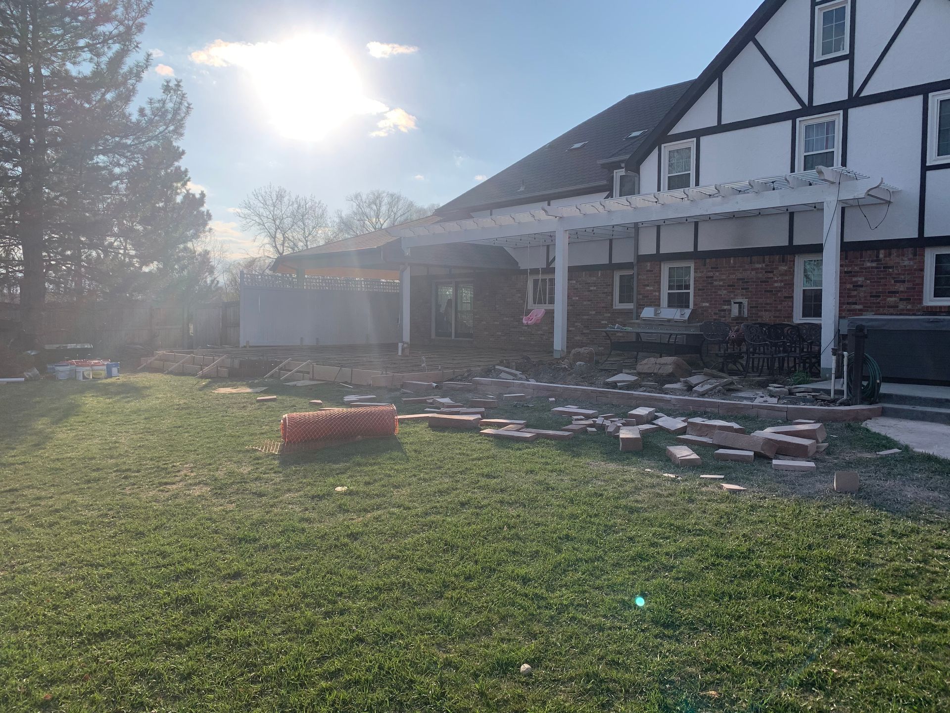 Backyard with pergola, red bricks scattered on grass, Tudor style house, sunny day.