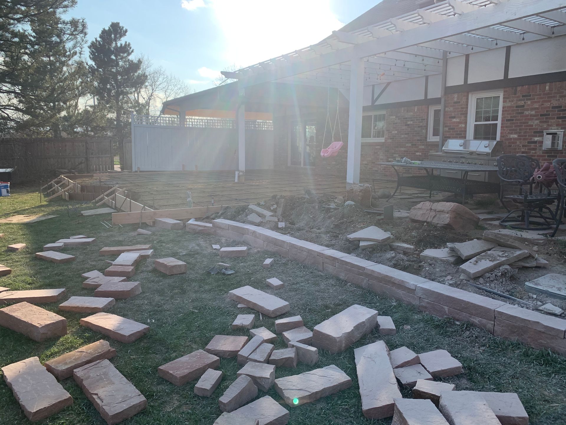 Backyard scene with scattered bricks, brick wall partially dismantled. White pergola and brick house visible.