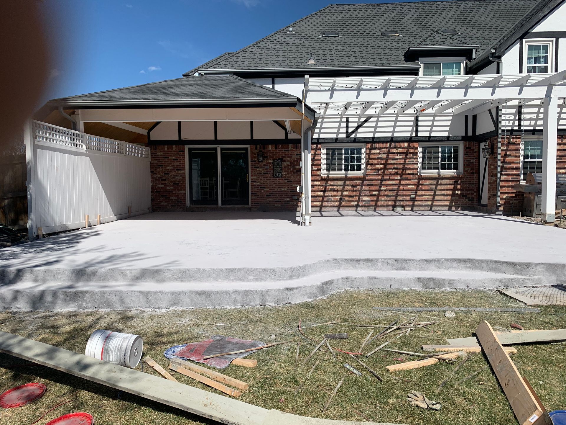 Backyard patio with a brick house, a pergola, and white concrete.