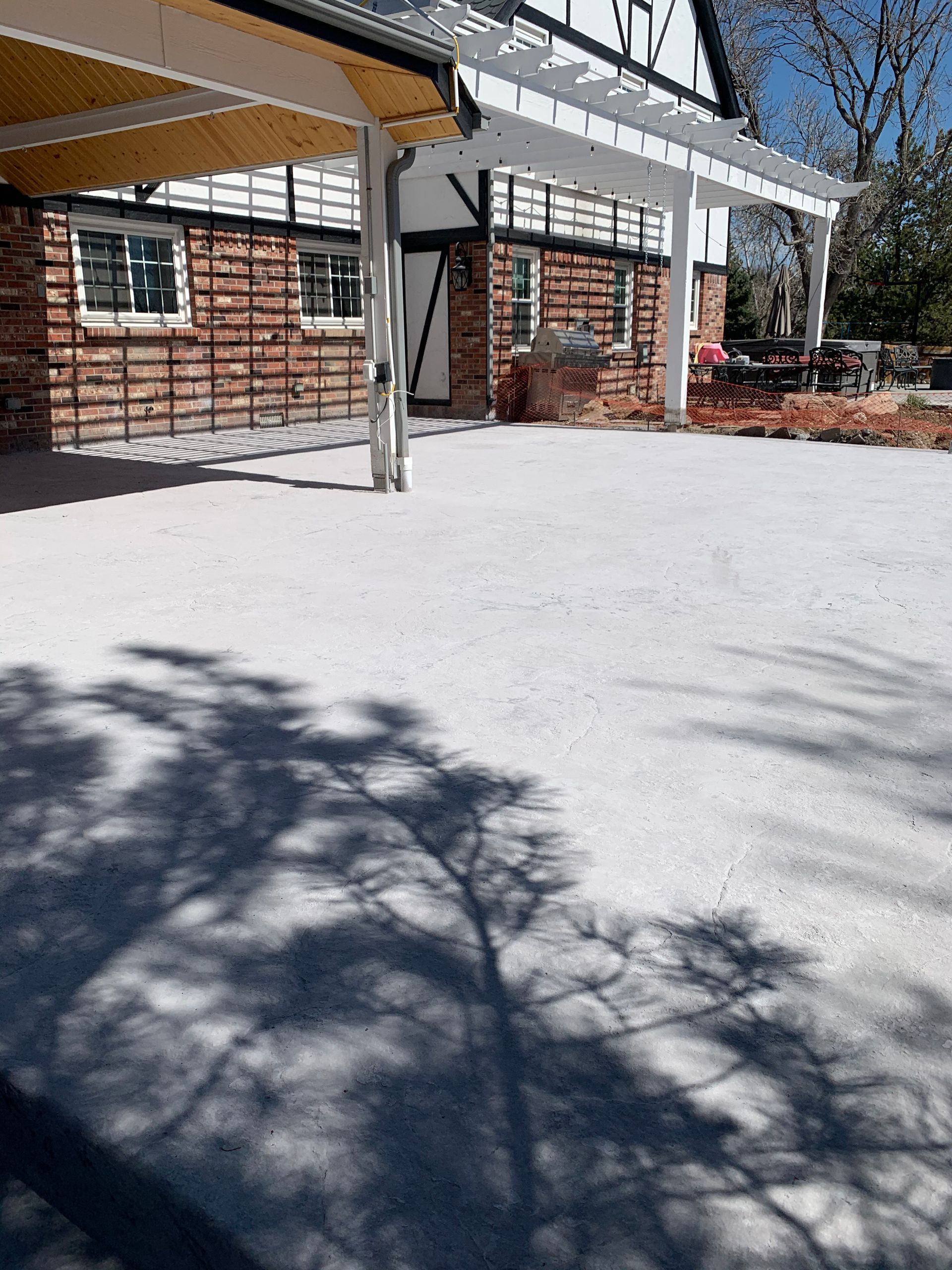 Exterior view of a brick and half-timbered building with a gravel patio; shadows of a tree fall on the ground.