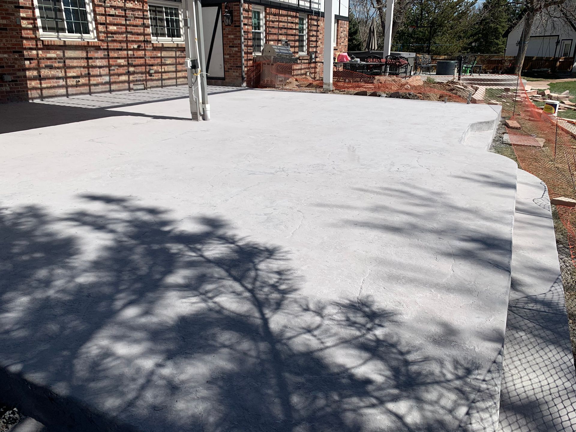 Newly poured concrete patio next to a brick building, with tree shadows.