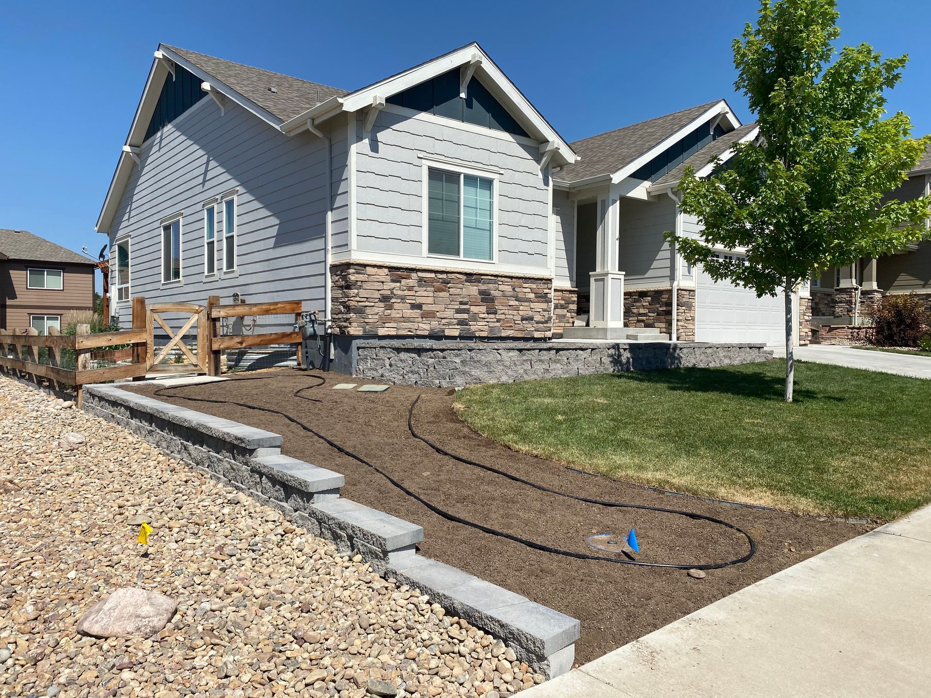 A blue house with gray siding, stone accents, and a small front yard with new irrigation system.
