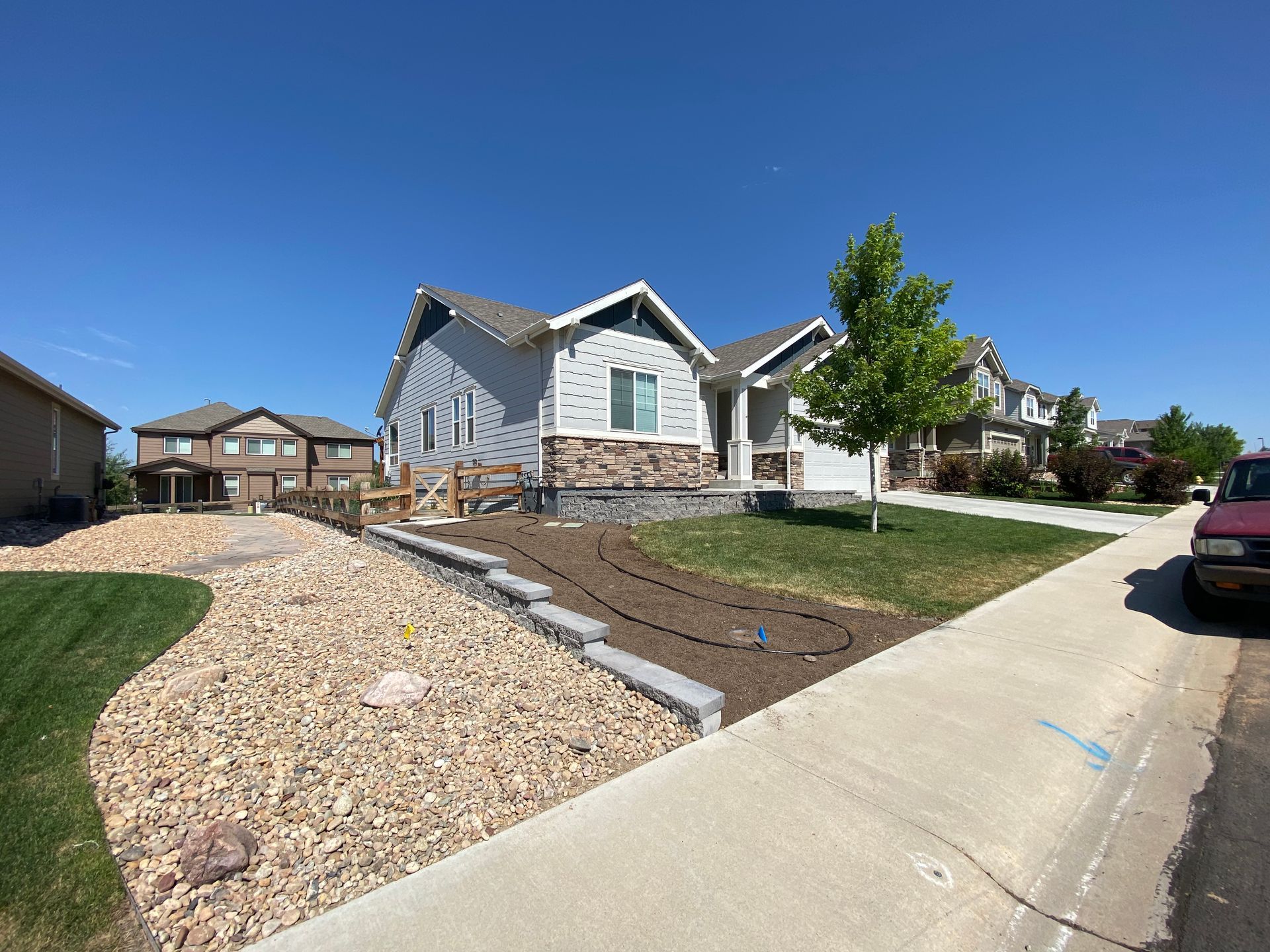 Gray house with stone accents and a gravel landscaping bed on a sunny street.