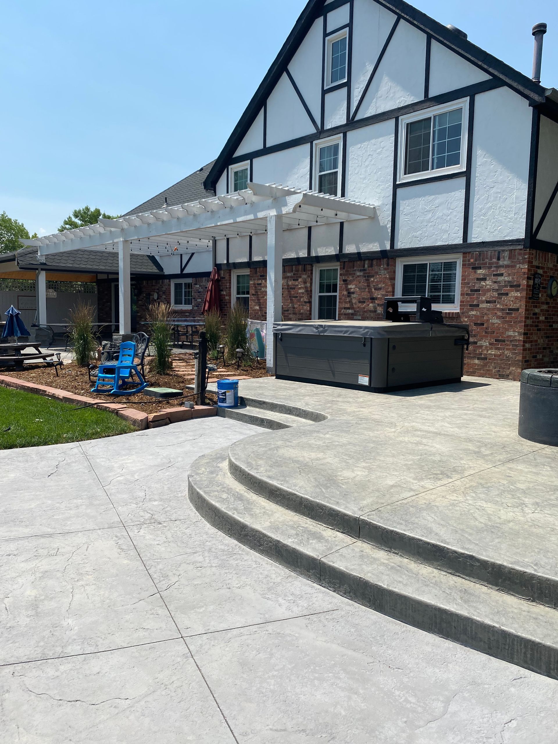 Backyard patio with hot tub, concrete steps, and a white pergola attached to a brick and stucco house.