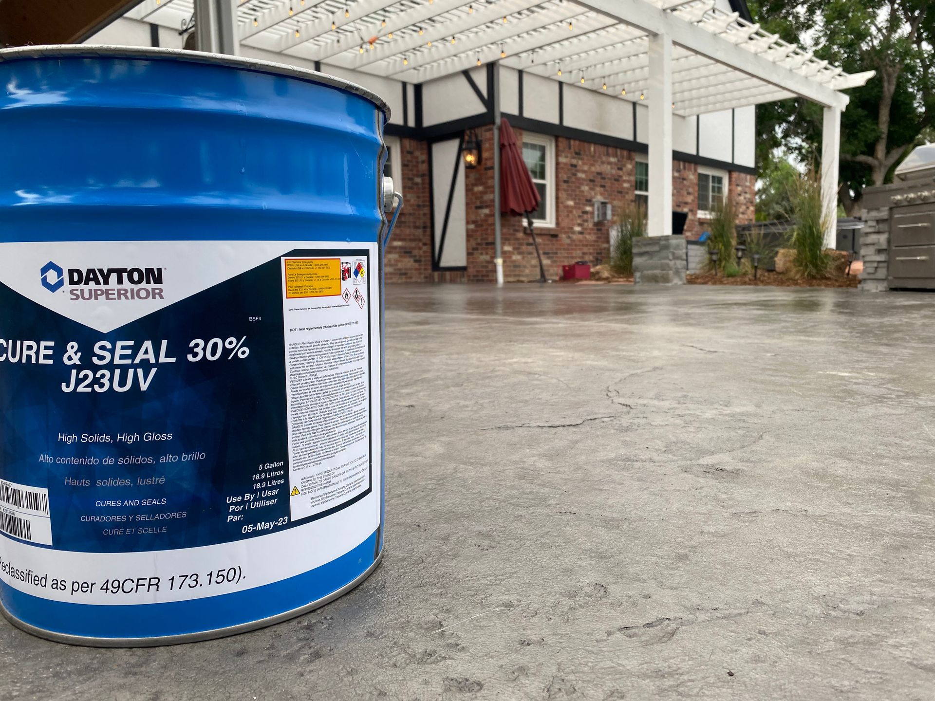 Blue Dayton Superior Cure & Seal 30% J23UV bucket on a concrete patio in front of a house.