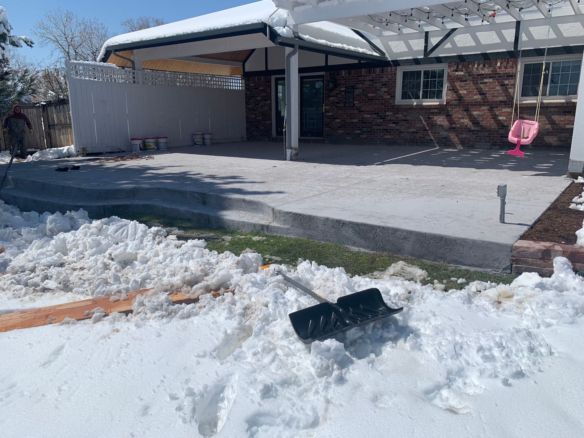 Backyard with fresh concrete patio, snow, and a snow shovel.