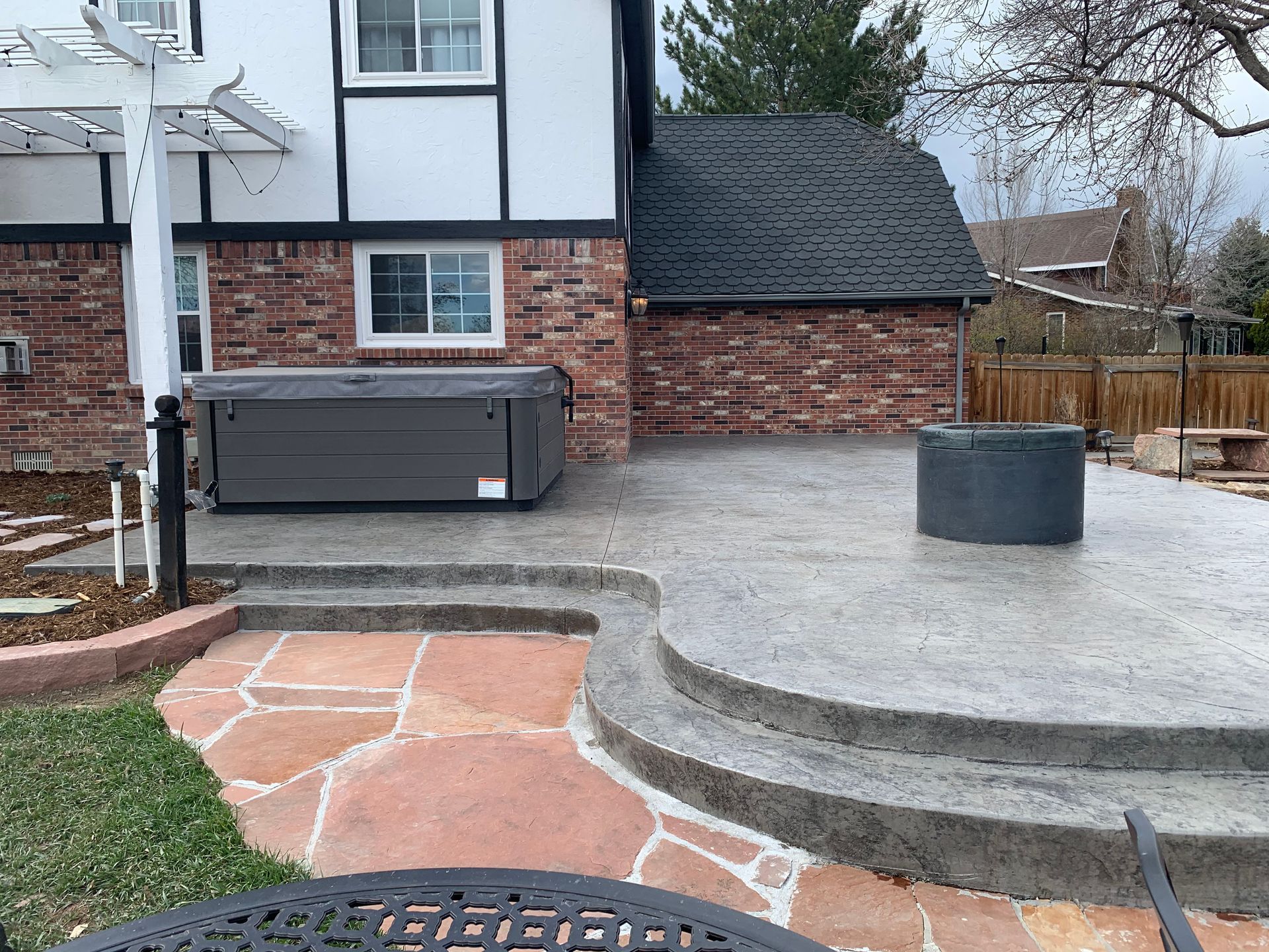 Backyard patio with hot tub, concrete steps, and red flagstone; gray and red brick house.