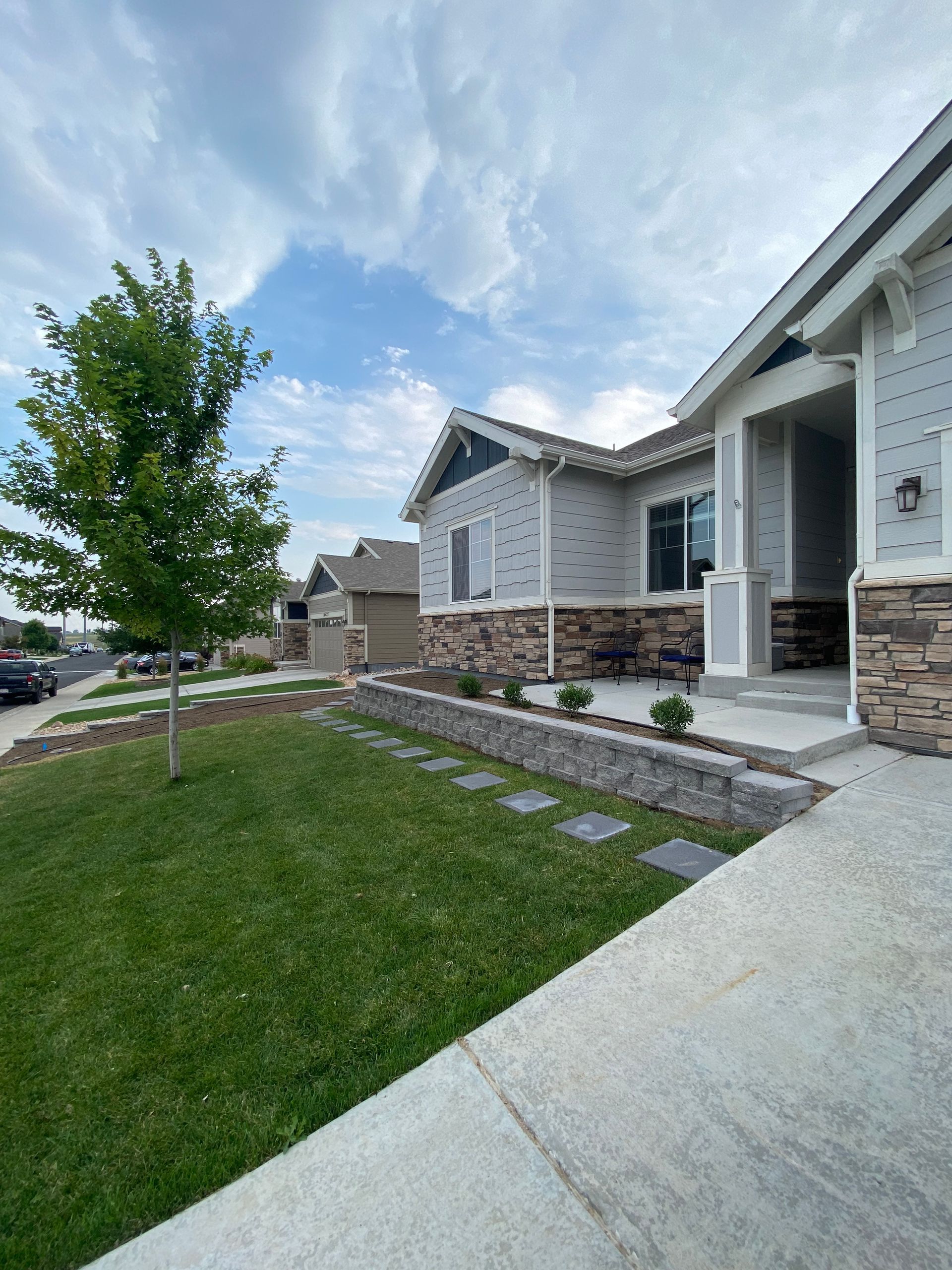 A house with a gray exterior, stone accents, and a sidewalk leading up to the front entrance. Green lawn and a small tree.