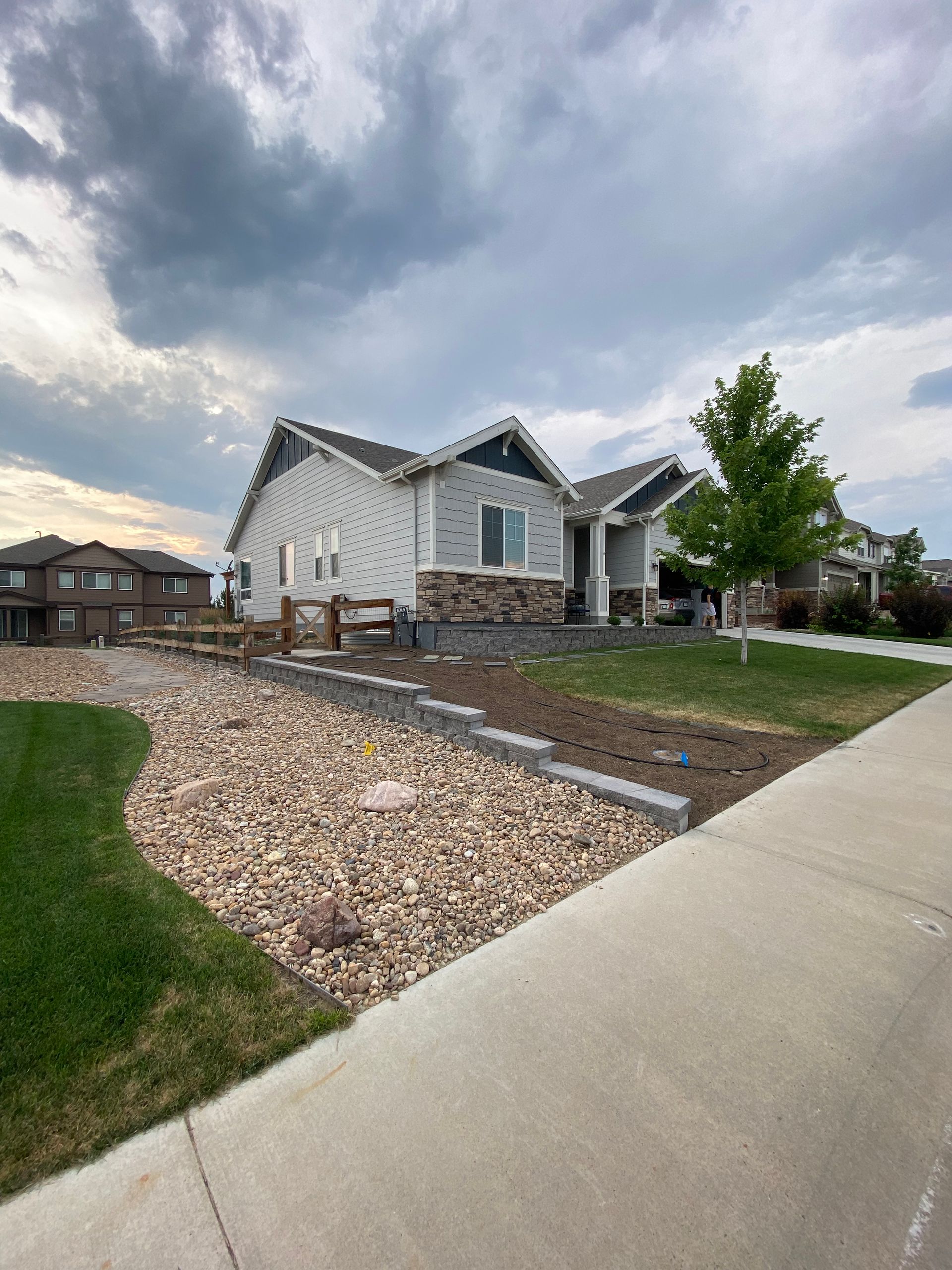 Light gray house with stone accents and rock landscaping under cloudy sky.