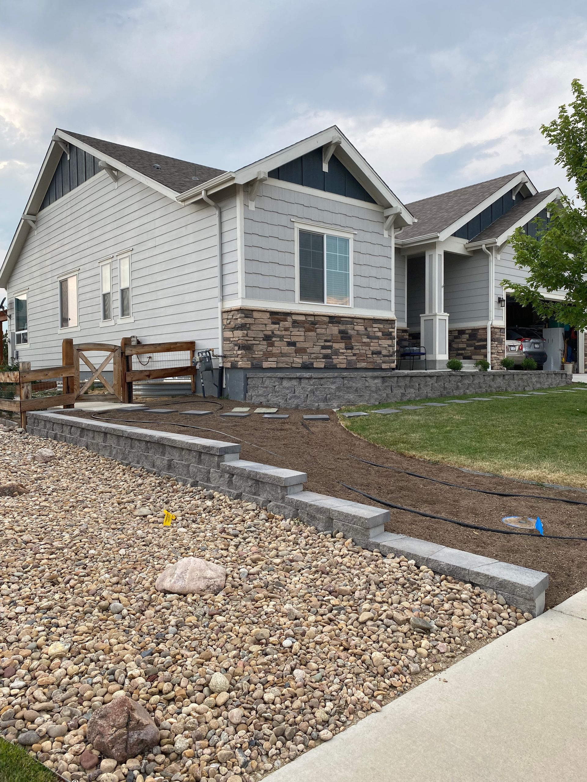 House with gray siding and stone accents, built into a slight hillside, with a rock retaining wall.