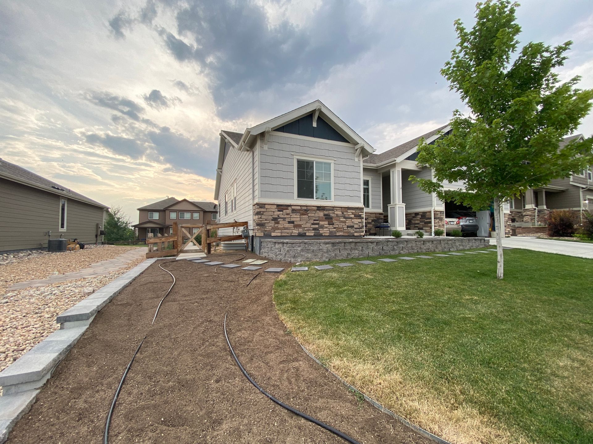 House exterior with gray siding, stone accents, green lawn, gravel path, and cloudy sky.