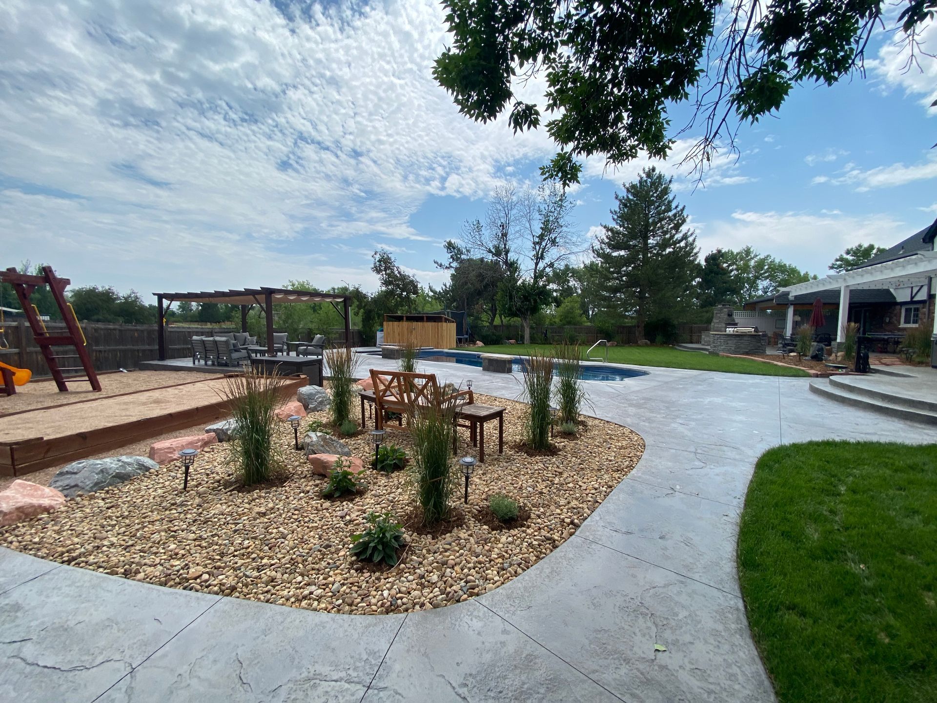 Spacious backyard with a pool, patio, playground, and landscaping under a cloudy sky.
