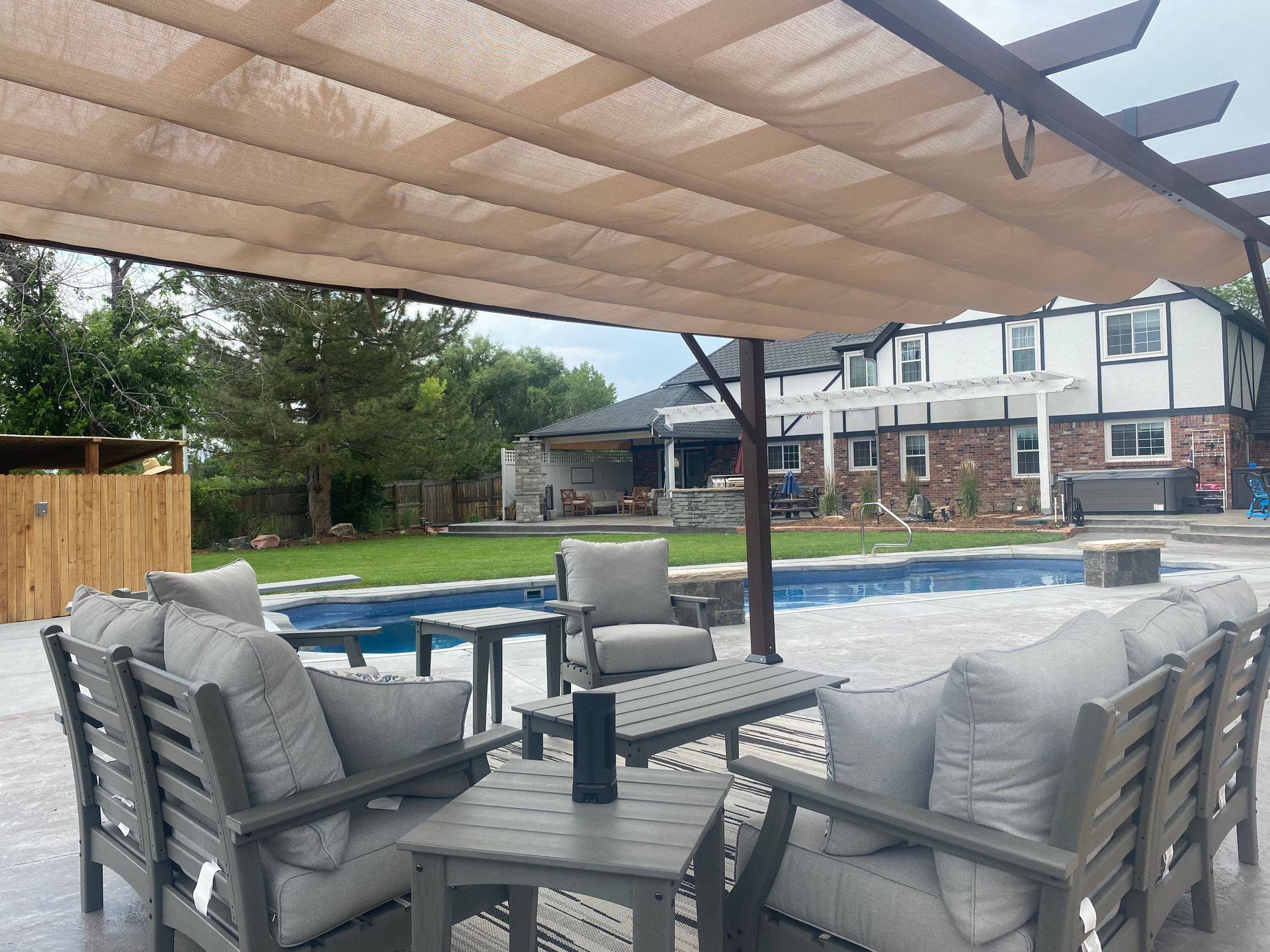 Patio with outdoor furniture, pool, and a beige retractable shade; a house in the background.
