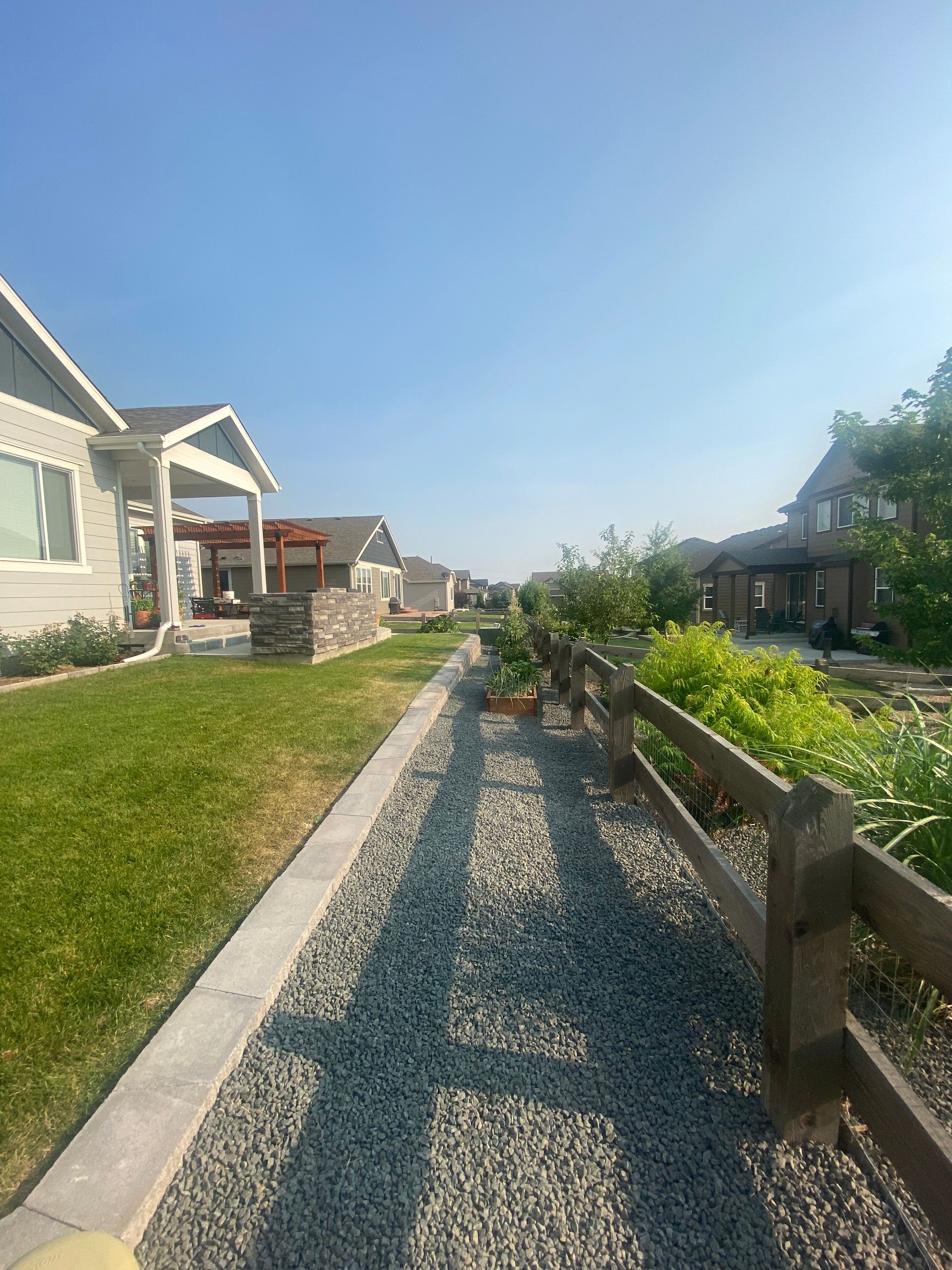 A gravel path with a wooden fence and houses on either side under a clear blue sky.