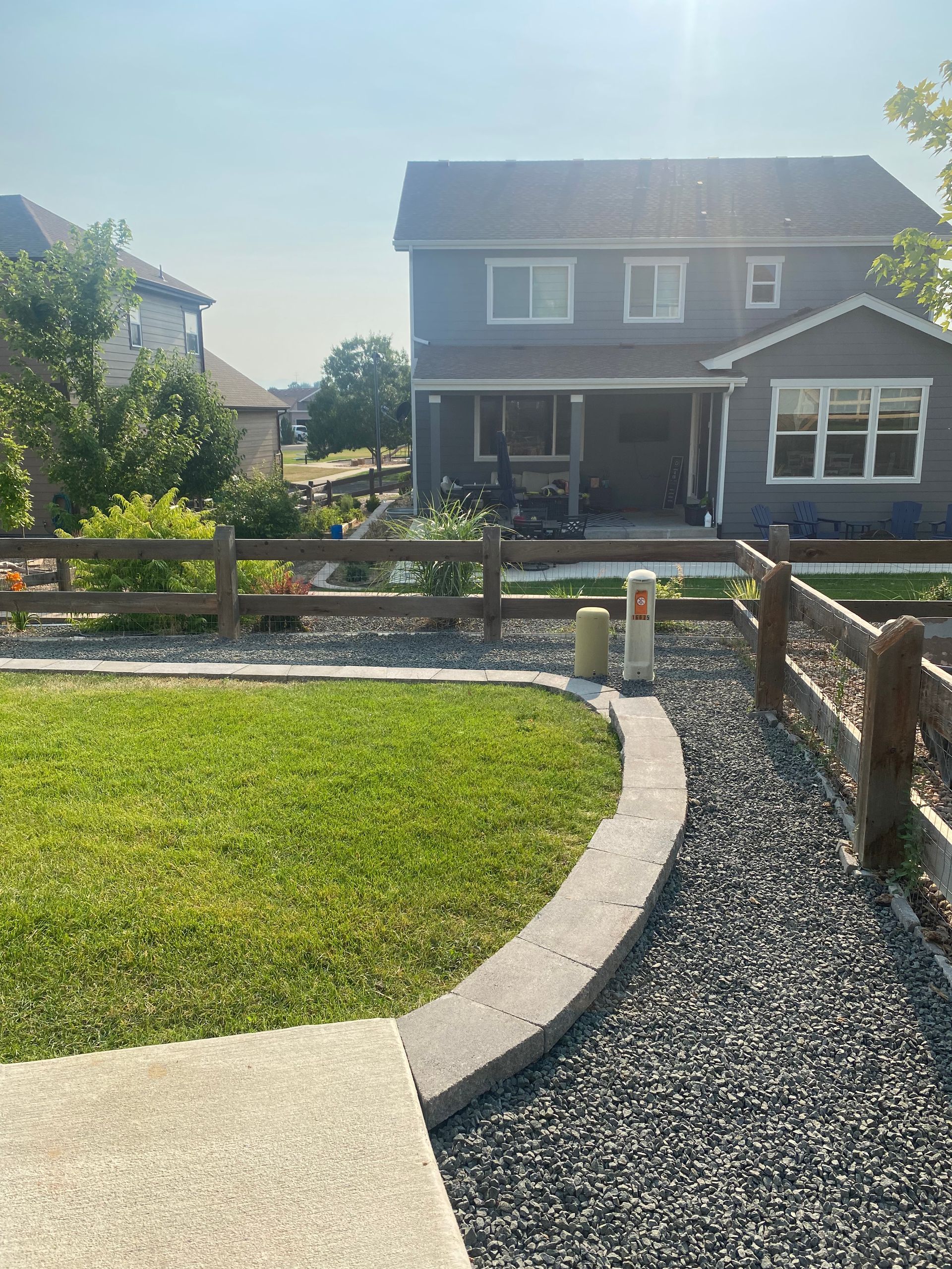 Lawn and gravel path leading to a two-story gray house with a wooden fence.