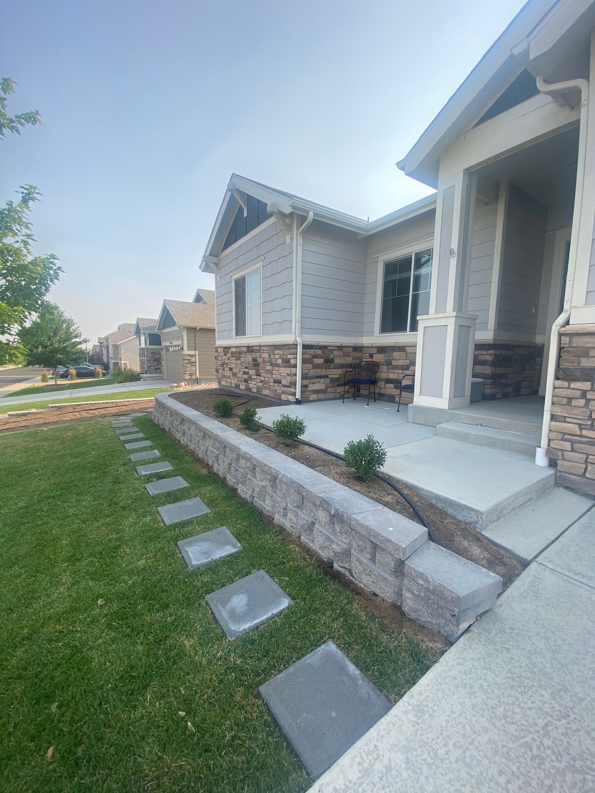 A house with a stone and tan exterior. A retaining wall and sidewalk lead to the entrance.