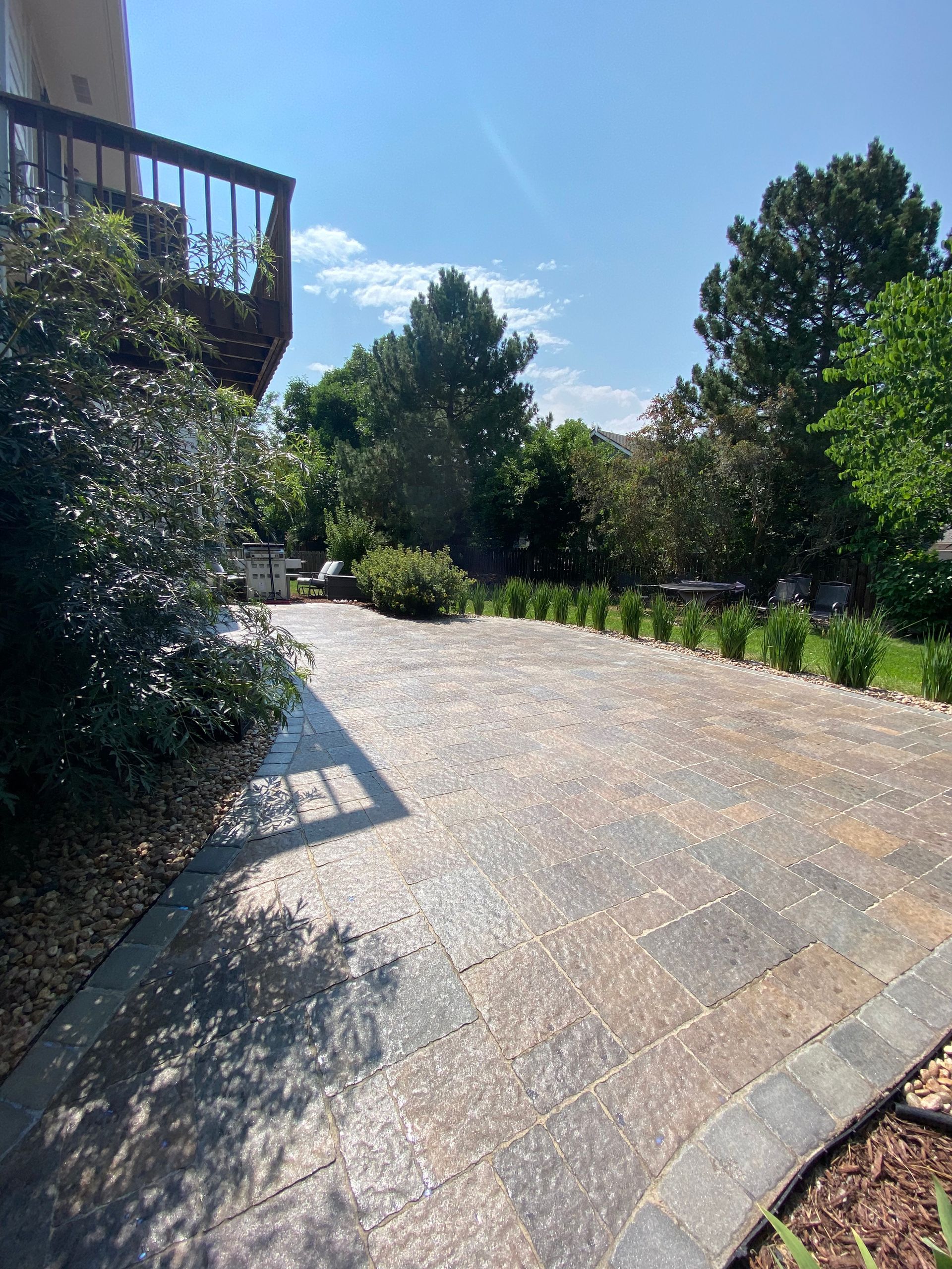 Brick patio with trees and a balcony on a sunny day.