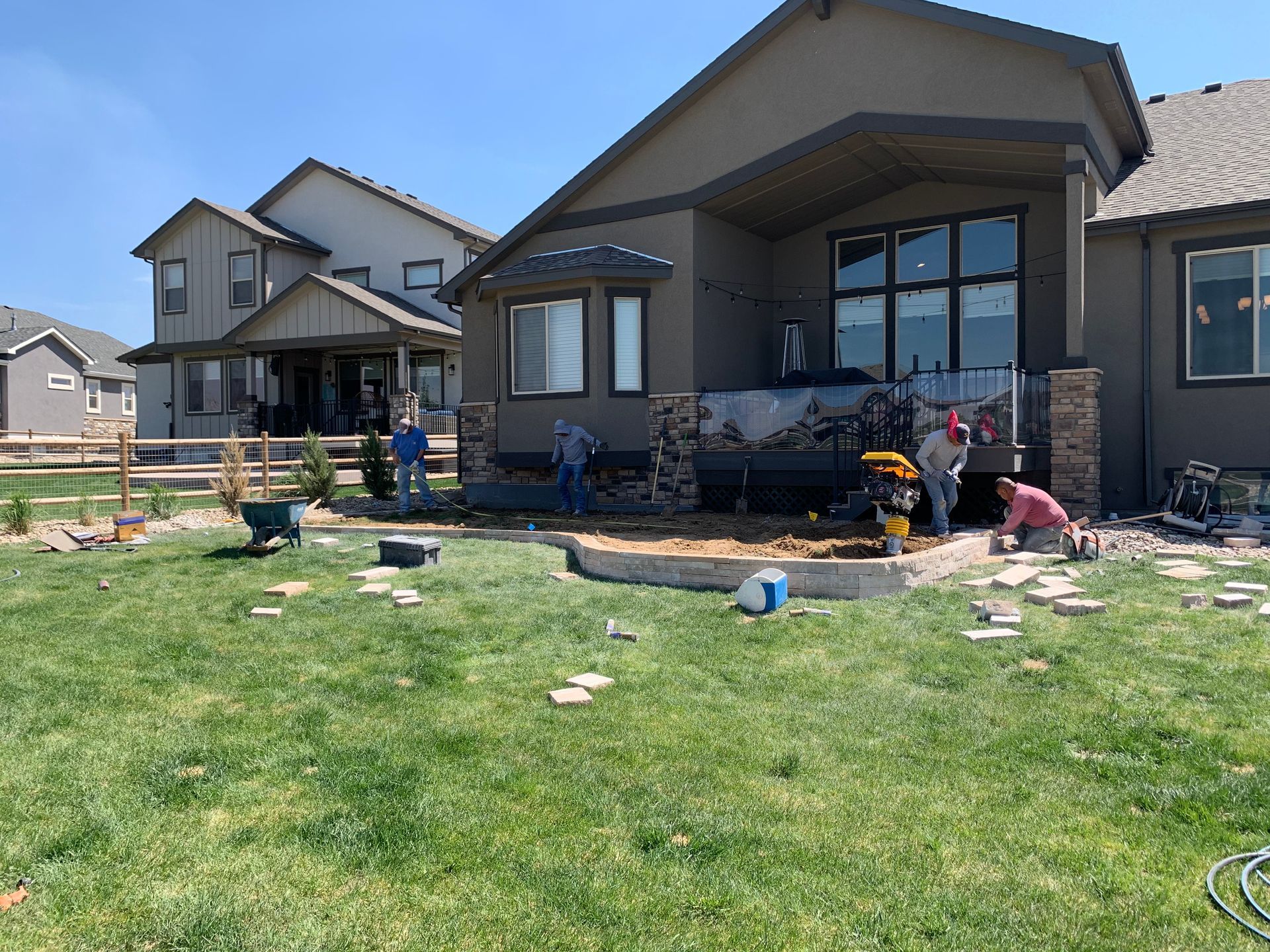 Workers installing stone landscaping in a backyard. House in the background. Green grass and blue sky.