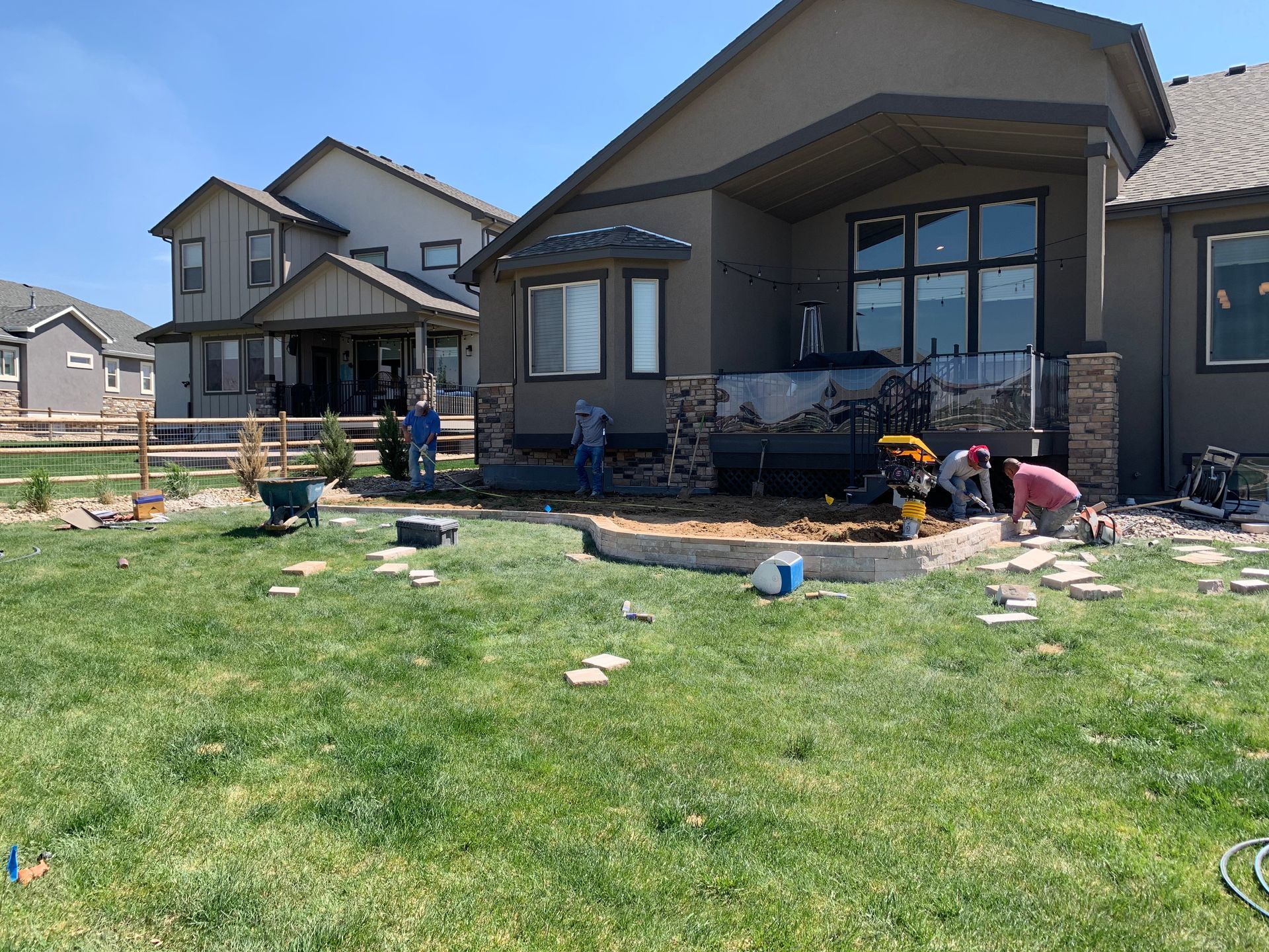 Backyard landscaping project with workers installing stonework near a house, sunny day.