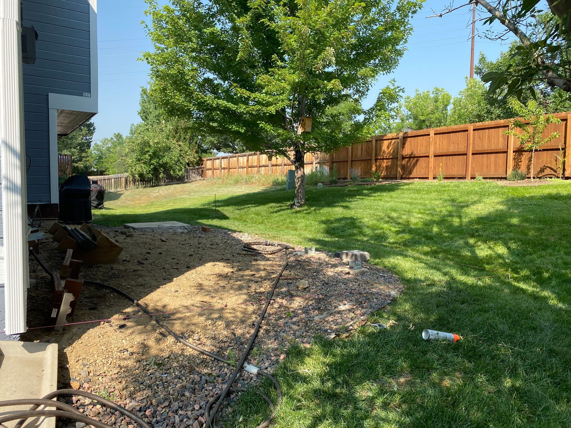 Backyard with gravel path, grassy lawn, tree, and wooden fence.