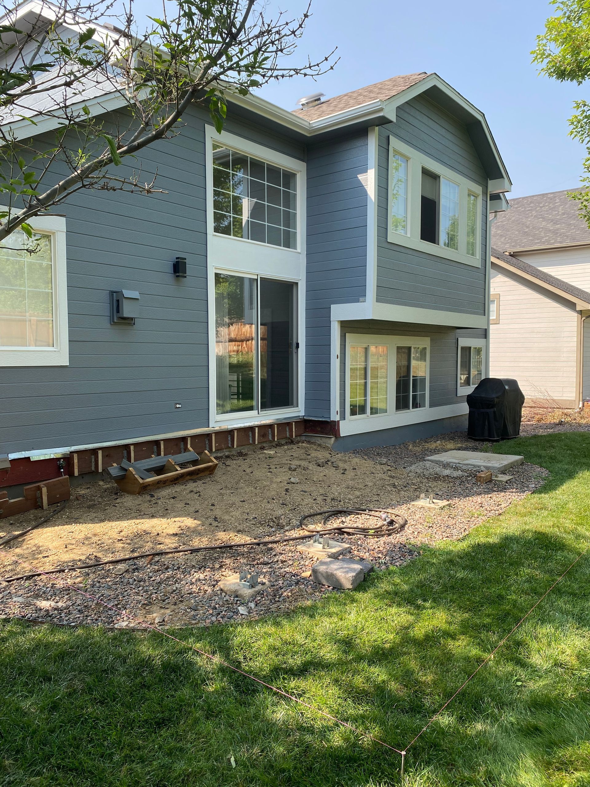 Two-story blue house exterior with gravel patio, windows, and green lawn.