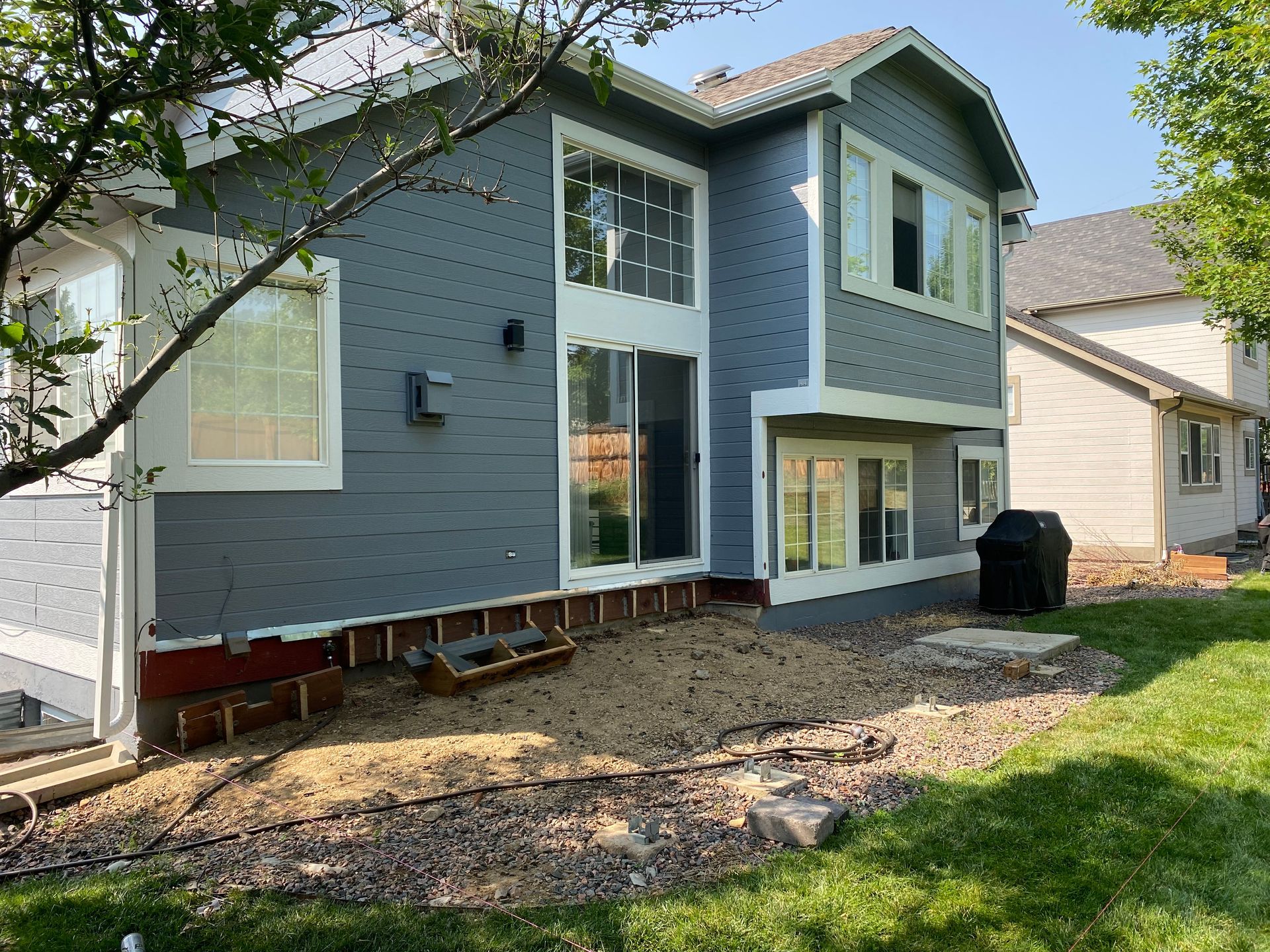 Back of a two-story blue house with white trim. Gravel ground. Green grass on the right.
