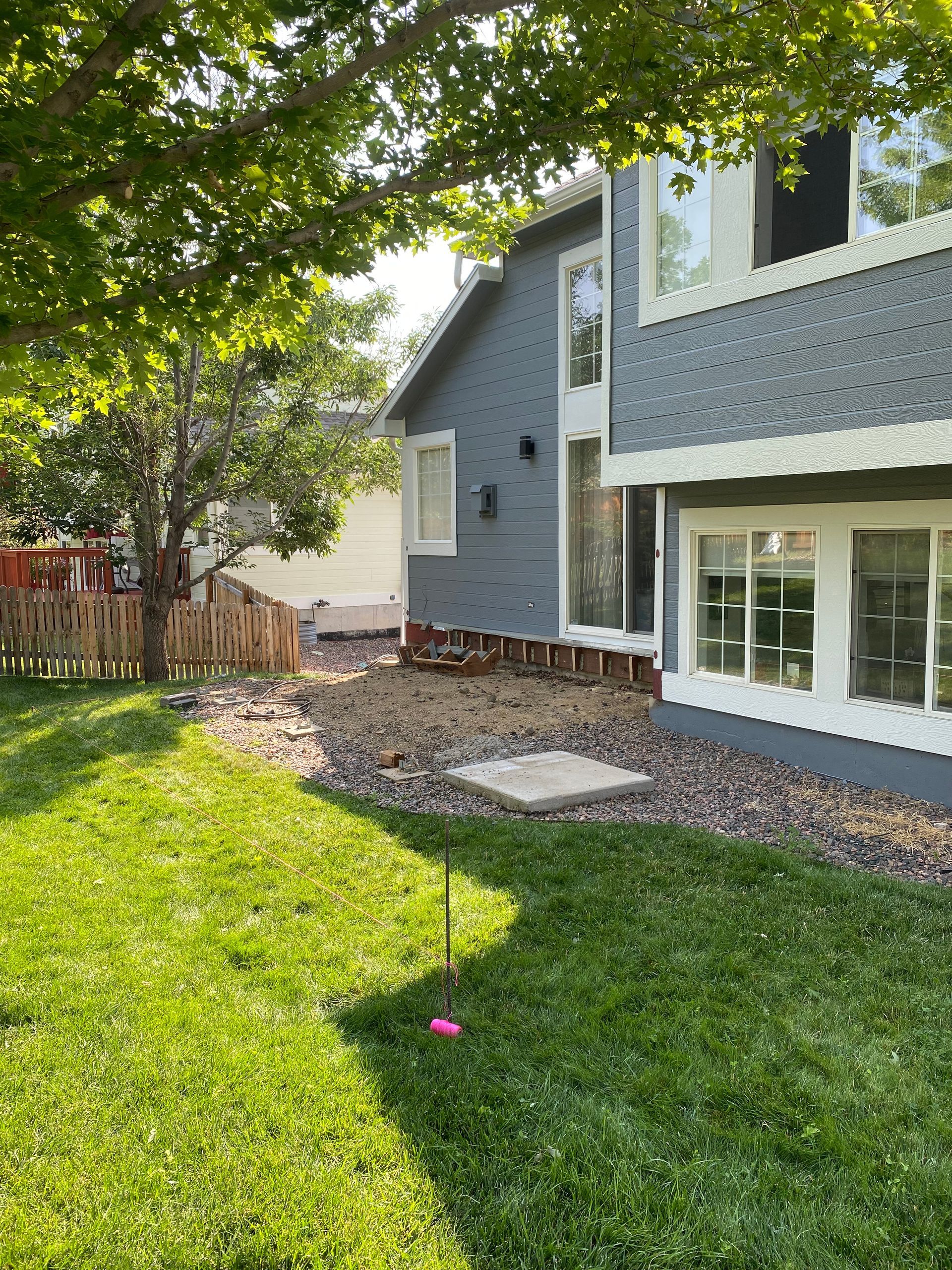 Side view of a blue house with a grassy lawn, rocky area, and wooden fence.